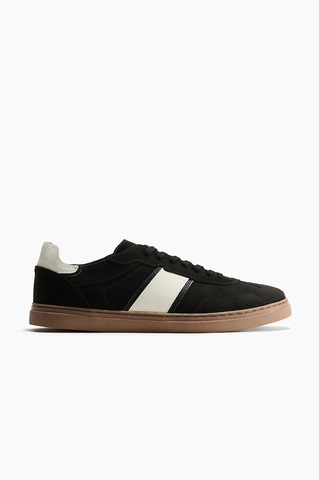 A black low-top sneaker is facing right in side profile, featuring a black suede upper with a wide diagonal off-white stripe on the side. The sneaker is designed with matching black laces, an off-white heel tab, and a contrasting brown gum outsole. - 1