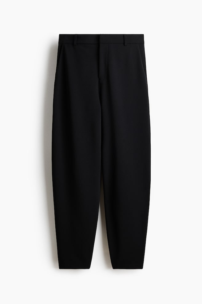 Black trousers crafted from a heavy jersey fabric are displayed in a front view, showcasing a high, elasticated waist with a zip fly and a concealed hook-and-bar fastening. They feature diagonal side pockets and barrel legs. - 1