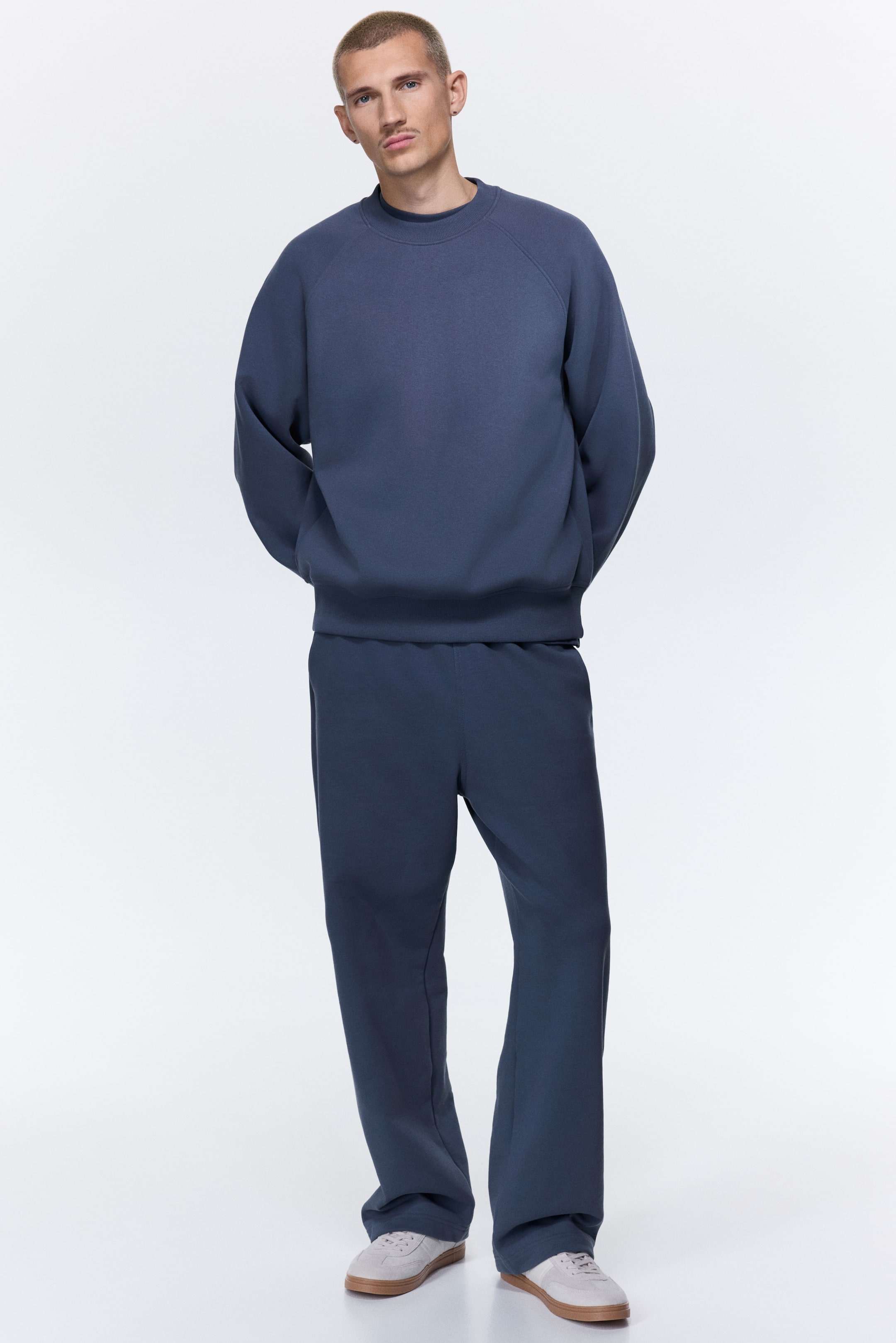 View larger image: A dark blue tracksuit is being shown, featuring a crew neck sweatshirt with raglan sleeves and a ribbed hem. The matching sweatpants are a relaxed, straight-leg style.