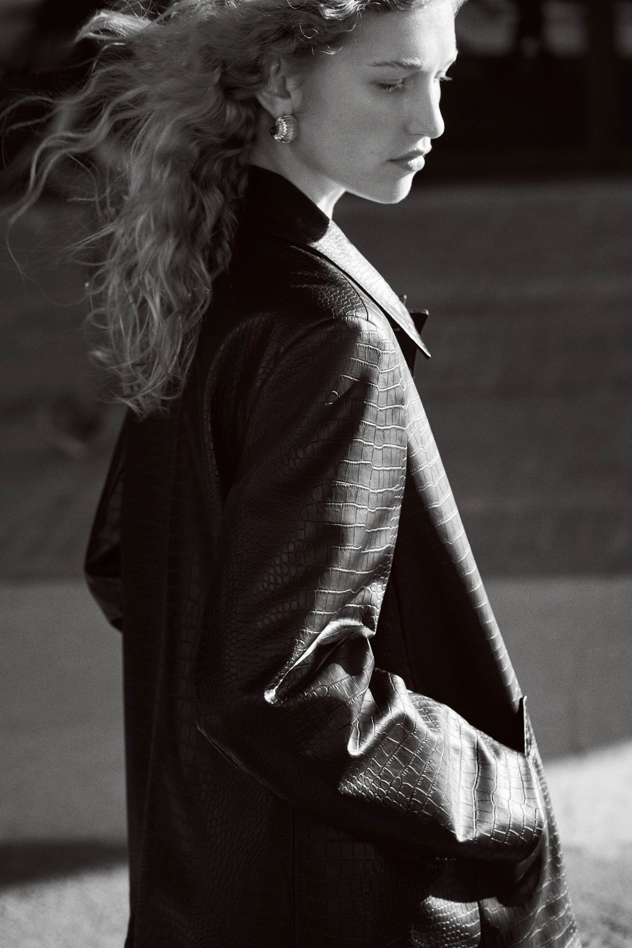 View larger image: A dark, crocodile-embossed jacket is being worn, seen from a side profile, featuring a structured shoulder, a notch lapel, and textured sleeves.