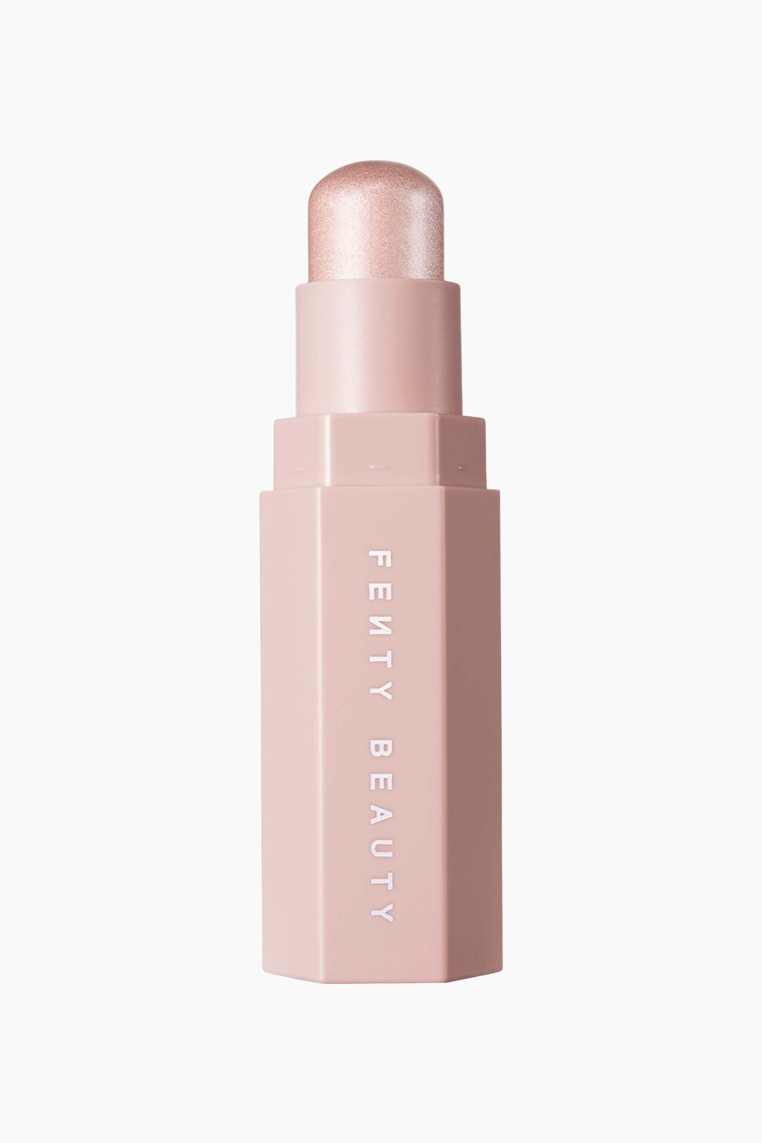 En Fenty Beauty-makeupstick stÃ¥r lodret og fremviser sit sekskantede, lyserosa etui med brandnavnet trykt lodret i hvidt. LÃ¥get er taget af og afslÃ¸rer en kuppelformet, skinnende lyserosa highlighter-stick Ã¸verst. - 1