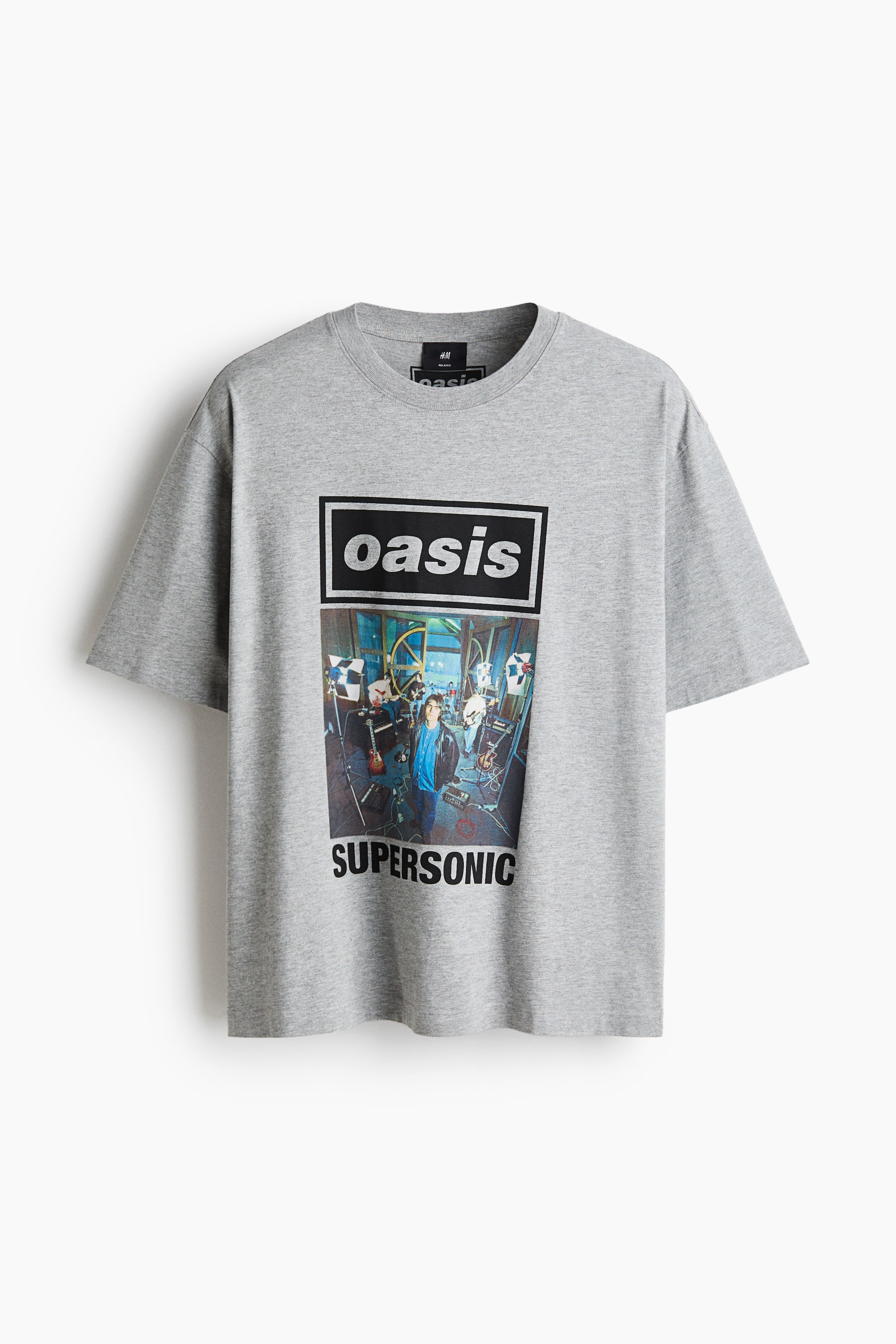 View larger image: A grey short-sleeved t-shirt is hanging, facing forward, featuring a graphic print on the front. The print is displaying "Oasis" in white text on a black rectangle, a colourful band photograph below it, and "Supersonic" in black text at the bottom.