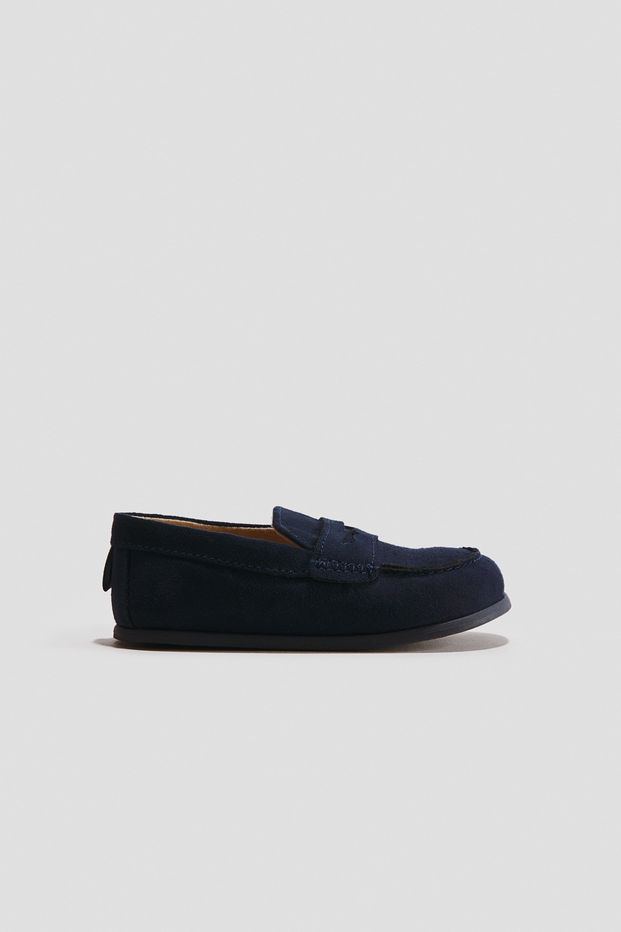 View larger image: Barefoot Loafers are shown in a side profile view facing right, featuring a navy blue suede upper with a classic penny keeper strap across the vamp. The shoe is displaying a moc-toe stitched detail, a thin, flexible flat black sole, and a tan interior lining.