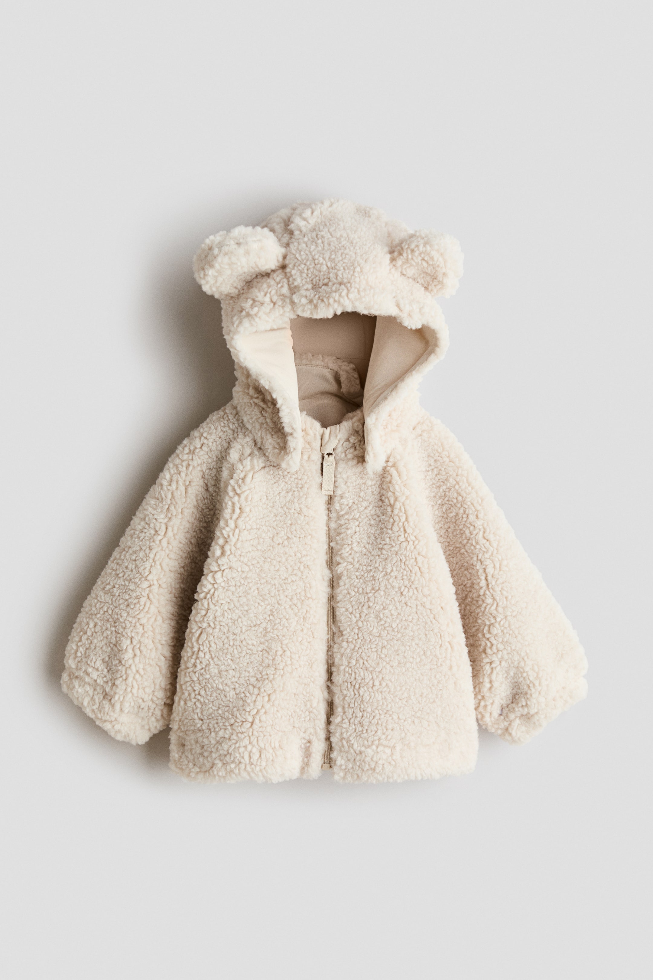 View larger image: The cream-coloured sherpa fleece jacket boasts a hooded design complete with two rounded ears, a full-length front zip closure with a rectangular pull tab, and elasticated cuffs and hem.