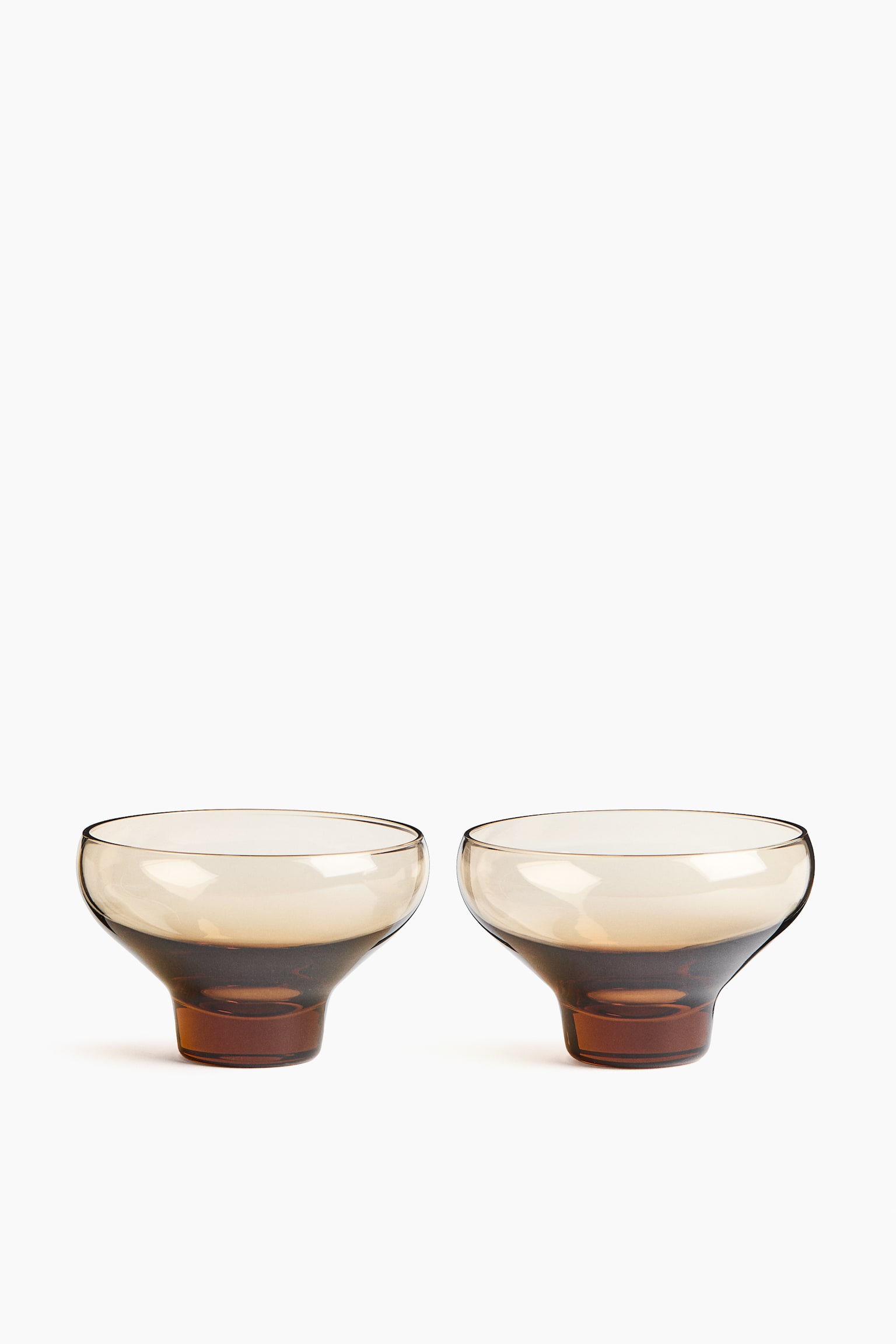 Two mouth-blown glass bowls are standing side-by-side, showcasing a wide, shallow cup design with a translucent amber-brown tint. Each bowl is tapering down to a thick, solid base displaying a deeper, more concentrated amber color.