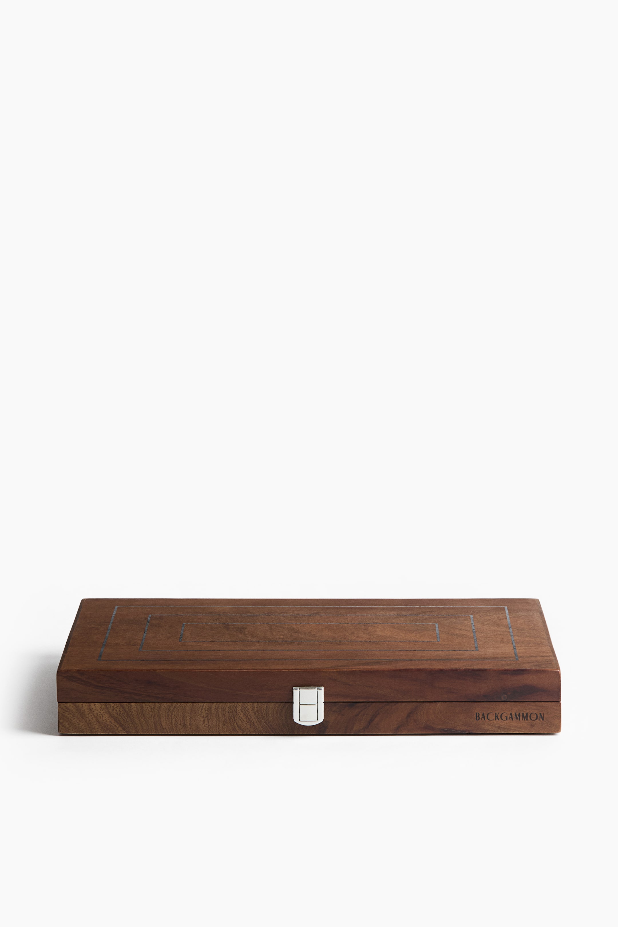View larger image: A closed wooden backgammon case is resting in a front-facing position, showcasing its rich brown woodgrain finish. The top lid features inlaid concentric rectangular lines, while a silver metal clasp secures the front centre, and the word "BACKGAMMON" appears on the bottom right edge.
