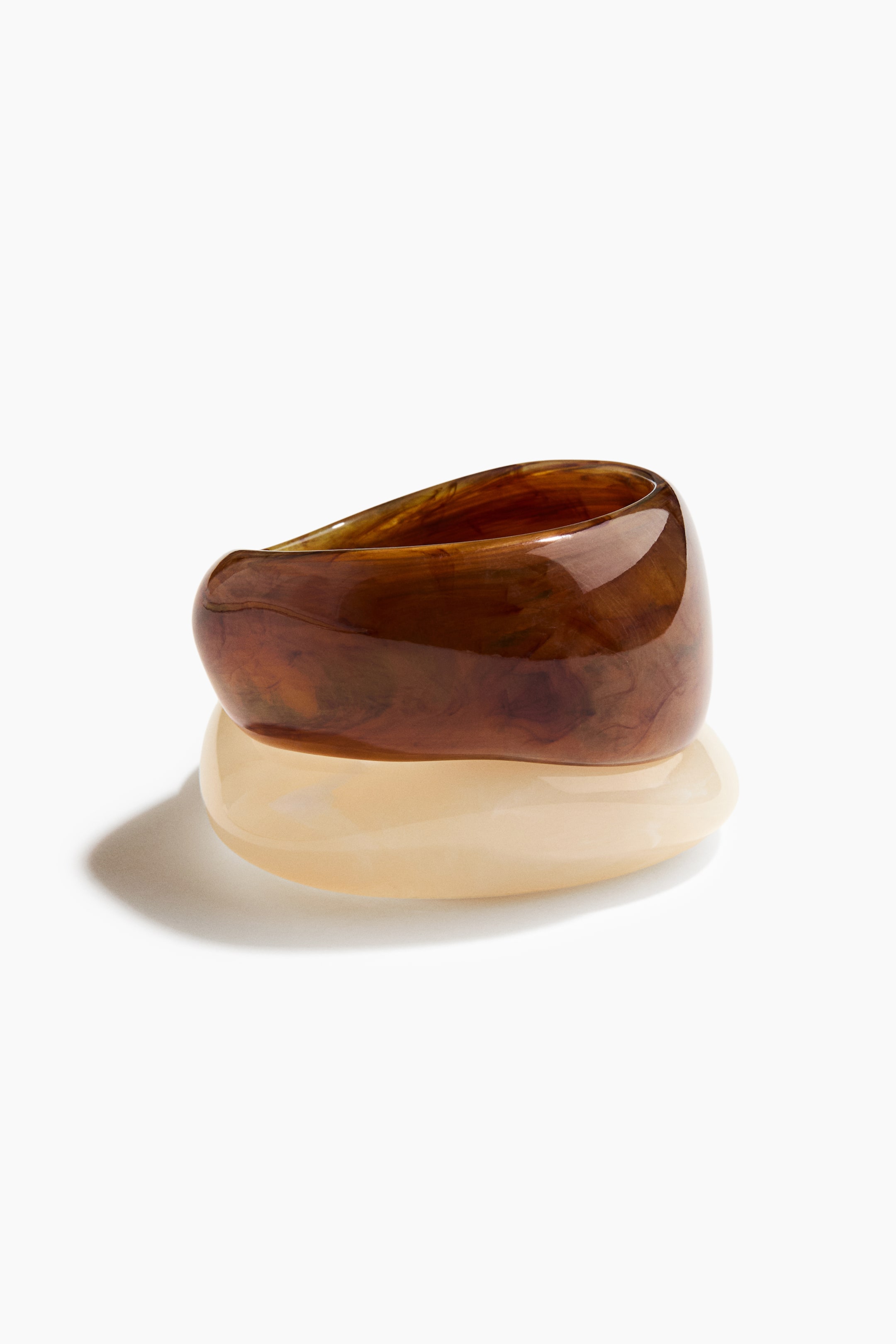 View larger image: Two bangles are stacking, with a glossy, dark brown, swirled bangle resting on top of a glossy, light beige bangle. Both bangles are displaying a thick, rounded, and slightly organic form, angled slightly forward.