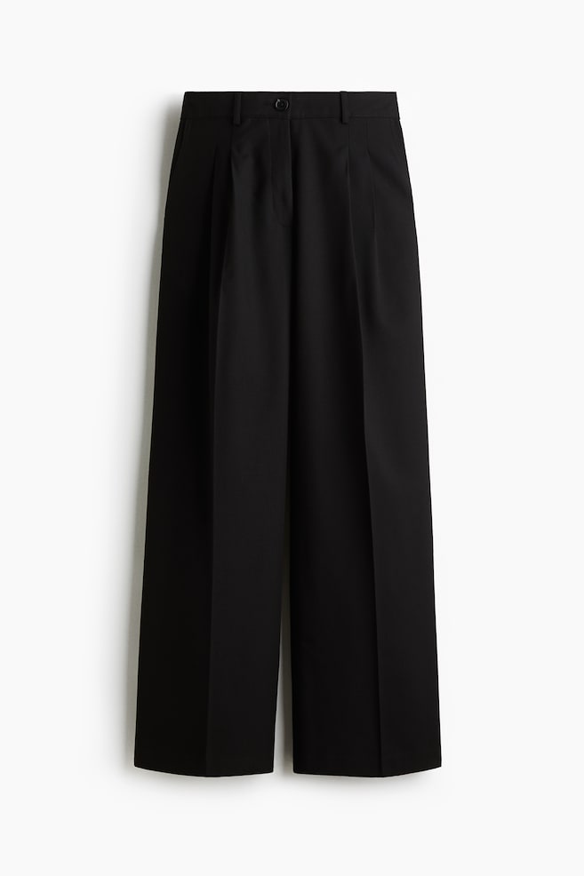 Black wide-leg pants are being presented from the front, featuring a flat waistband with belt loops, a single button and zip fly closure, and two front pleats on each leg. Side pockets and crisp vertical creases are also visible. - 1
