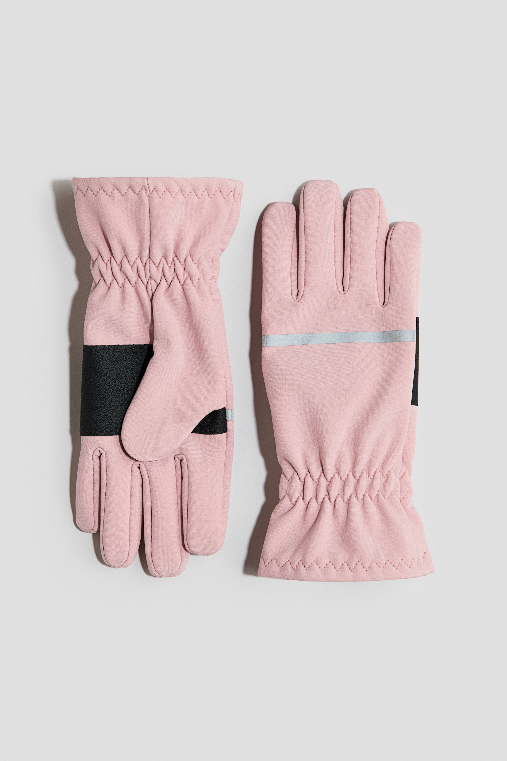 Ver imagen más grande: Un par de guantes rosados presenta muñecas elásticas con tela fruncida. Un guante muestra su palma con un refuerzo texturizado negro, mientras que el otro exhibe el dorso de la mano con una tira horizontal reflectante plateada.