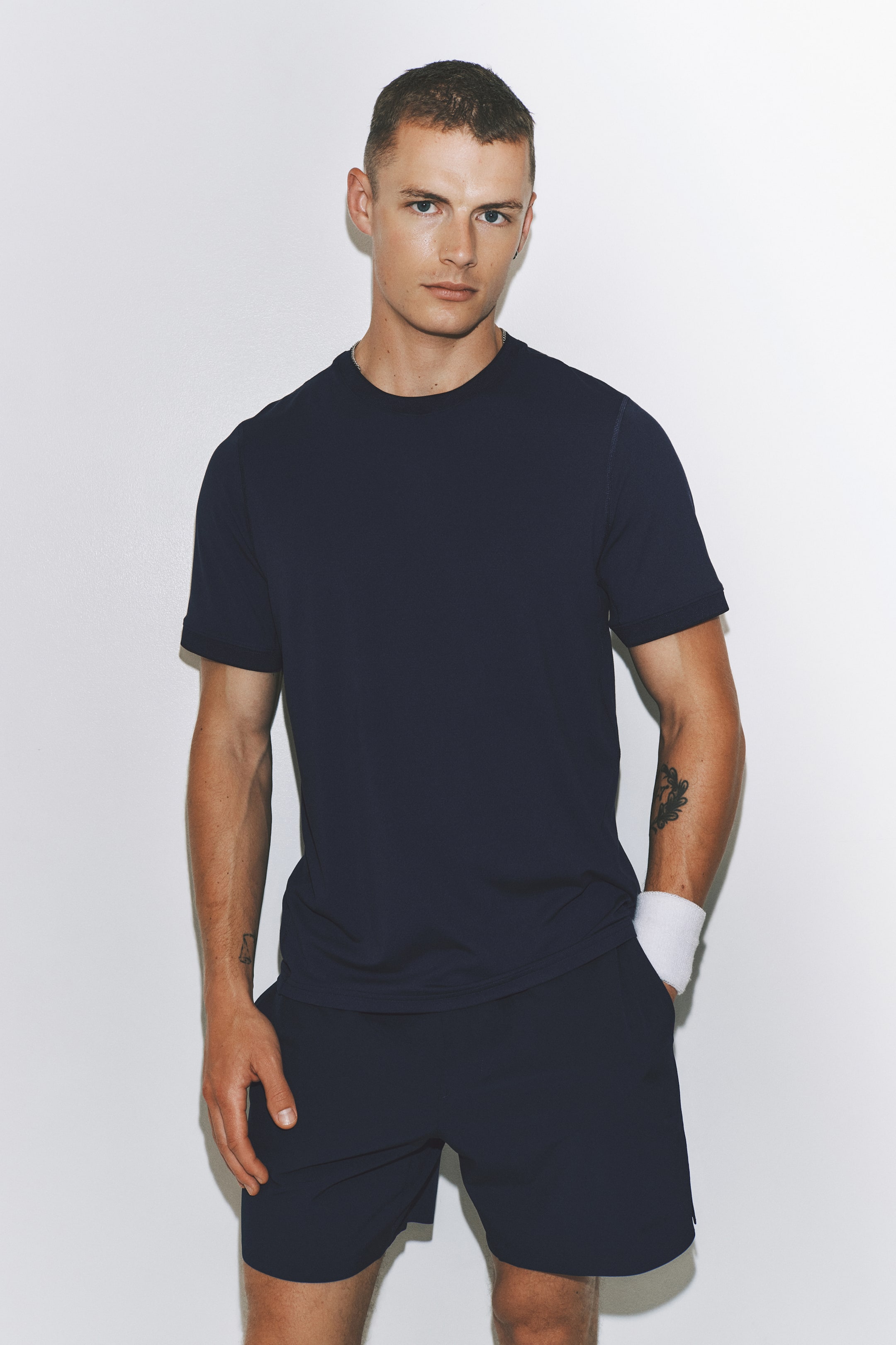Voir une image plus grande: Un t-shirt bleu marine à manches courtes et col rond est porté, avec des coutures visibles au niveau de l'encolure et des épaules. Il est assorti à un short de sport bleu marine, qui repose au-dessus du genou.
