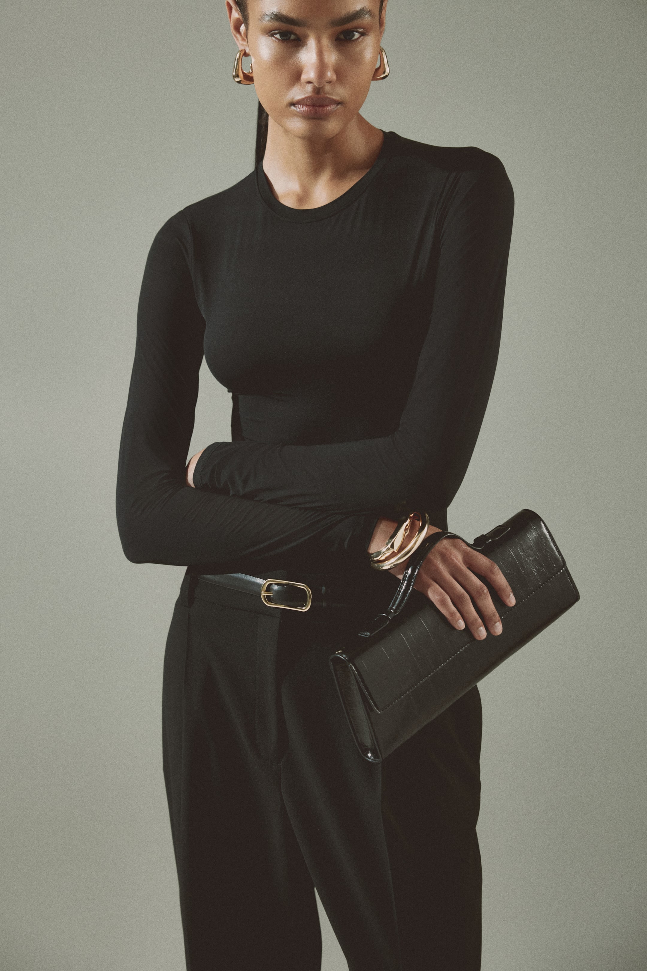 View larger image: The black long-sleeve top features a crew neck and a form-fitting silhouette. It's styled tucked into black trousers.