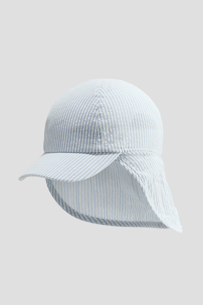 A sun cap, depicted from the front, is crafted from a light blue and white striped soft cotton weave. It features a peak at the front, covered elastication at the back, and a flap extending down to shield the back of the neck. - 1