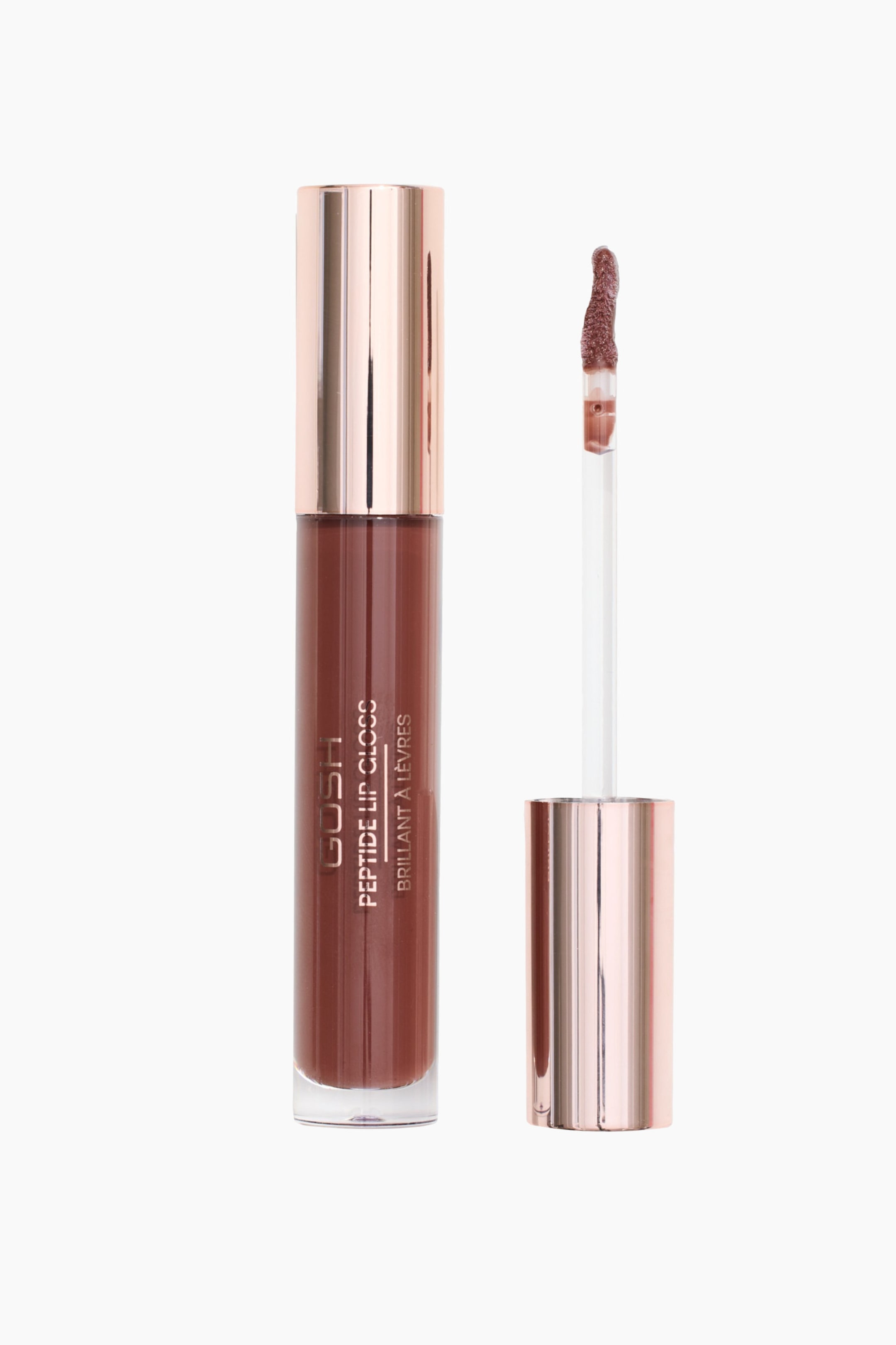 Näytä suurempi kuva: Sylinterimäinen GOSH Peptide Lip Gloss -putki seisoo pystyasennossa sen vieressä olevan irrotetun levityskynän vieressä. Läpinäkyvä putki näyttää sen sisällä olevan pölyisen ruusunruskean huulikiillon, ja sitä kruunaa metallinhohtoinen ruusukultainen korkki, kun taas viereisessä kynässä on sitä vastaava ruusukultainen varsi sekä kaareva, glossilla päällystetty doe-foot-applikaattorikärki.