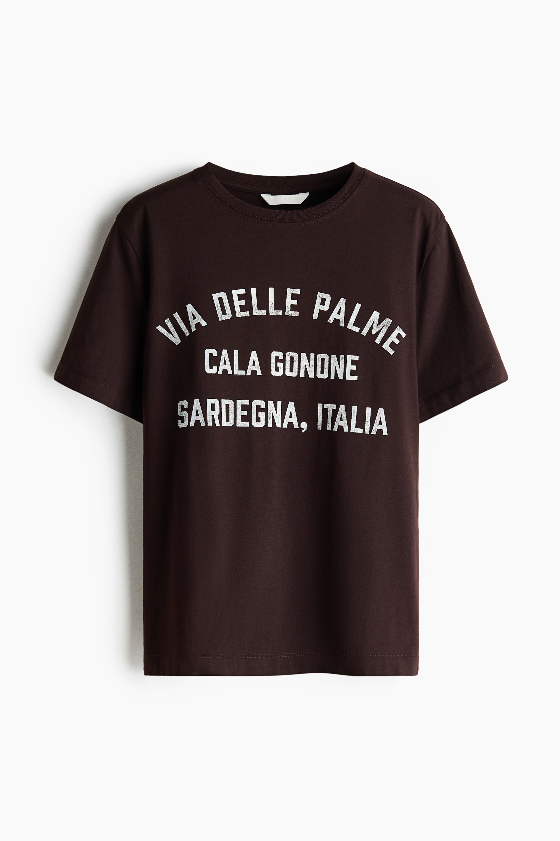 View larger image: A classic dark brown cotton jersey t-shirt is showcased front-facing, featuring a round neckline, short sleeves, and a straight-cut hem. It displays a white distressed print on the front chest, reading 'VIA DELLE PALME' in an arch, followed by 'CALA GONONE' and 'SARDEGNA, ITALIA' in straight lines.