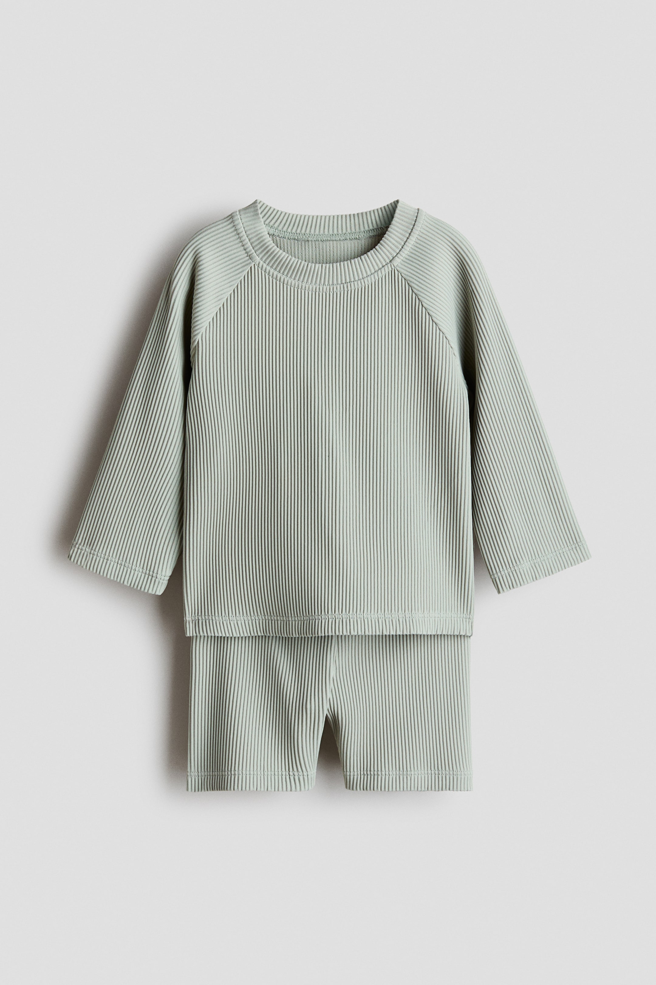 查看大圖: 淺綠色的條紋游泳上衣和配套短褲從正面平放展示。 上衣具有圓領和長款拉格蘭袖，而短褲則展示了鬆緊腰設計。