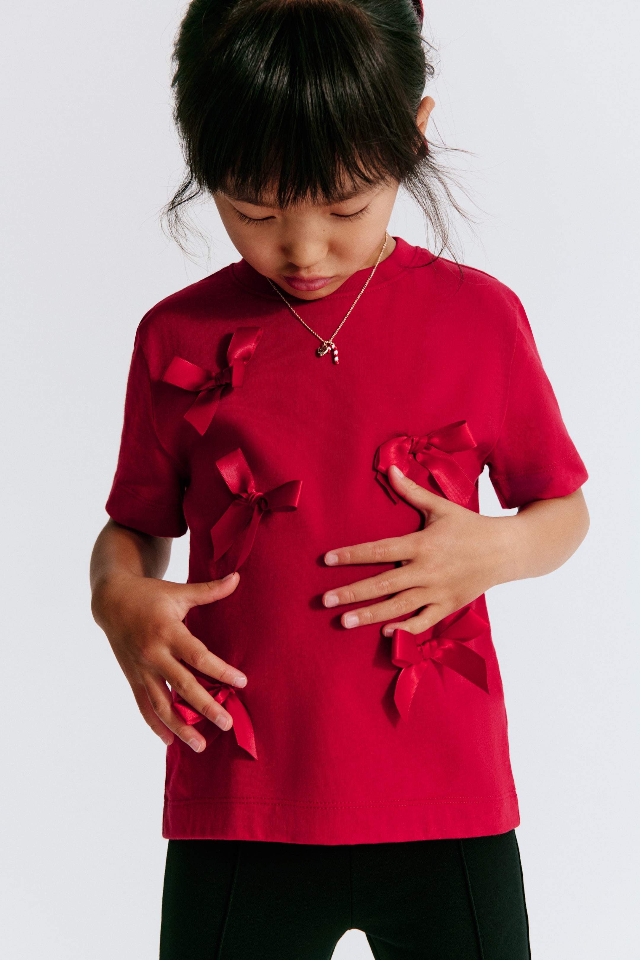 View larger image: A red, short-sleeve crewneck T-shirt is shown from the front, featuring multiple matching red satin bows appliquéd across the front.
