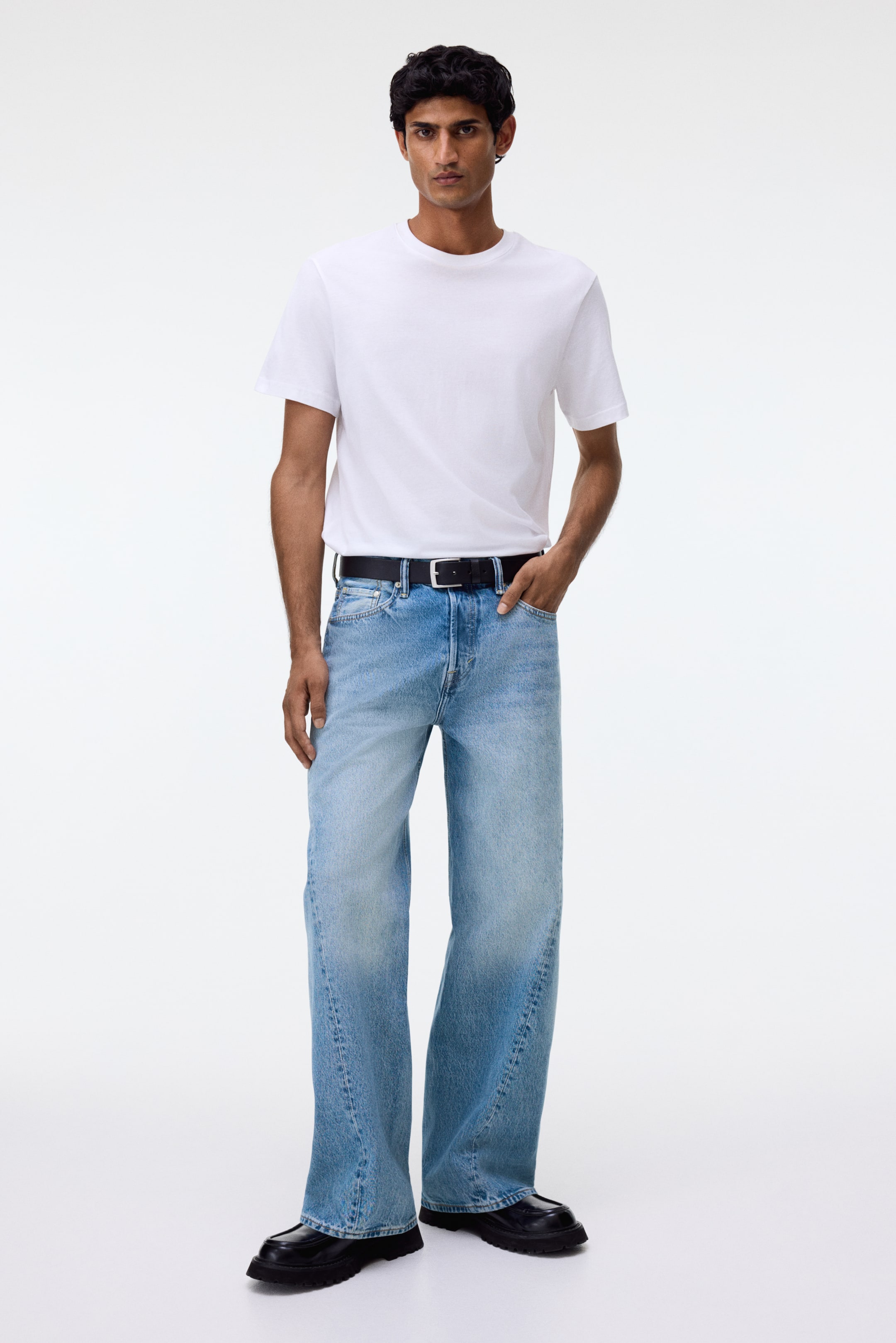 View larger image: Light blue, wide-leg jeans are being presented in a full-body front view, showing a high-waisted, loose fit with a faded wash. They feature visible front pockets, a button-fly closure, and are styled with a black belt through the belt loops. The wide hems are pooling over black shoes.