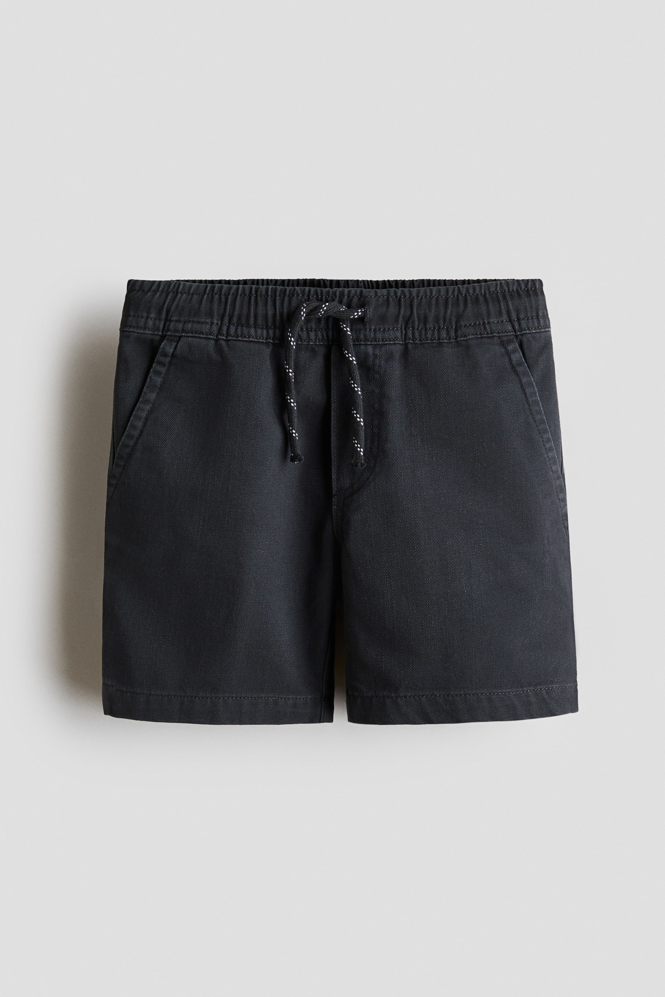 Ver imagen más grande: Pantalones cortos hasta la rodilla en un tejido de algodón gris oscuro vistos desde el frente. Presentan una cintura elástica con cordón ajustable de color negro y blanco moteado, una bragueta falsa y bolsillos laterales diagonales.