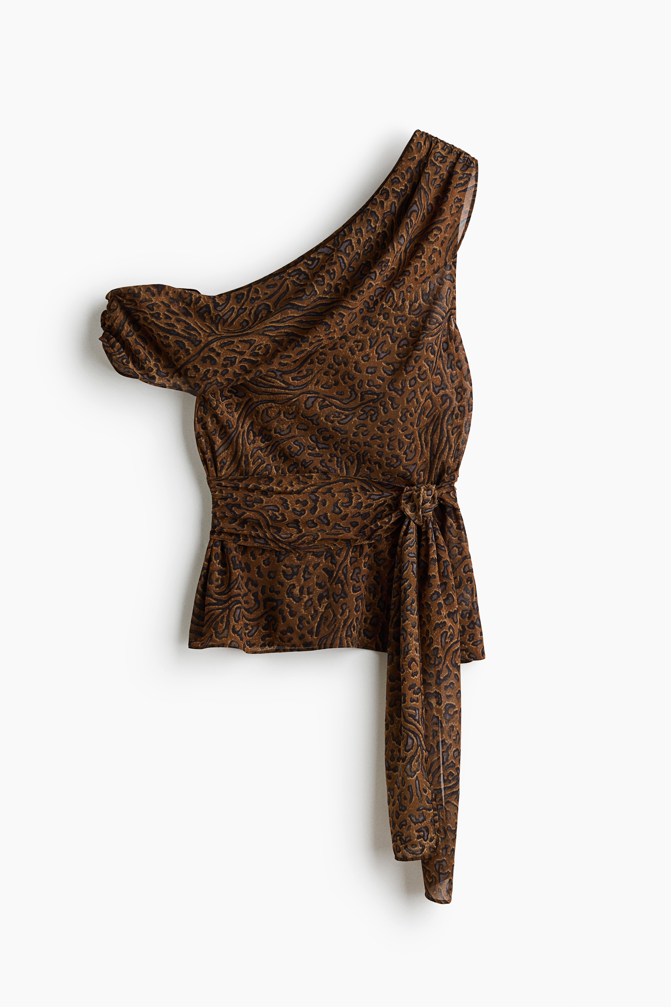 Een chiffon top met Ã©Ã©n schouder in een bruine dierenprint wordt gedragen door het model, met een gedrapeerde, asymmetrische halslijn en een bijpassende tailleriem met een lange sjerp die aan de voorkant naar beneden hangt. De top is gestyled met losse, witte wide-leg broeken.