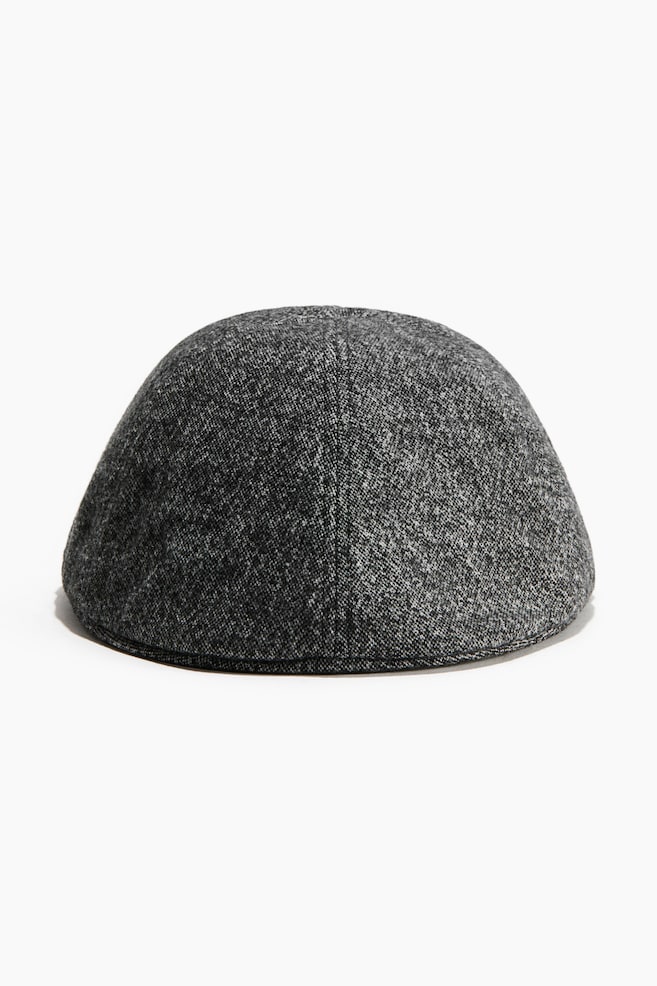 Eine Flatcap zeigt eine abgerundete, kuppelfÃ¶rmige Krone in einem gesprenkelten, schwarz-grau strukturierten Gewebe, von hinten mit einer vertikalen Mittelnaht dargestellt. - 1