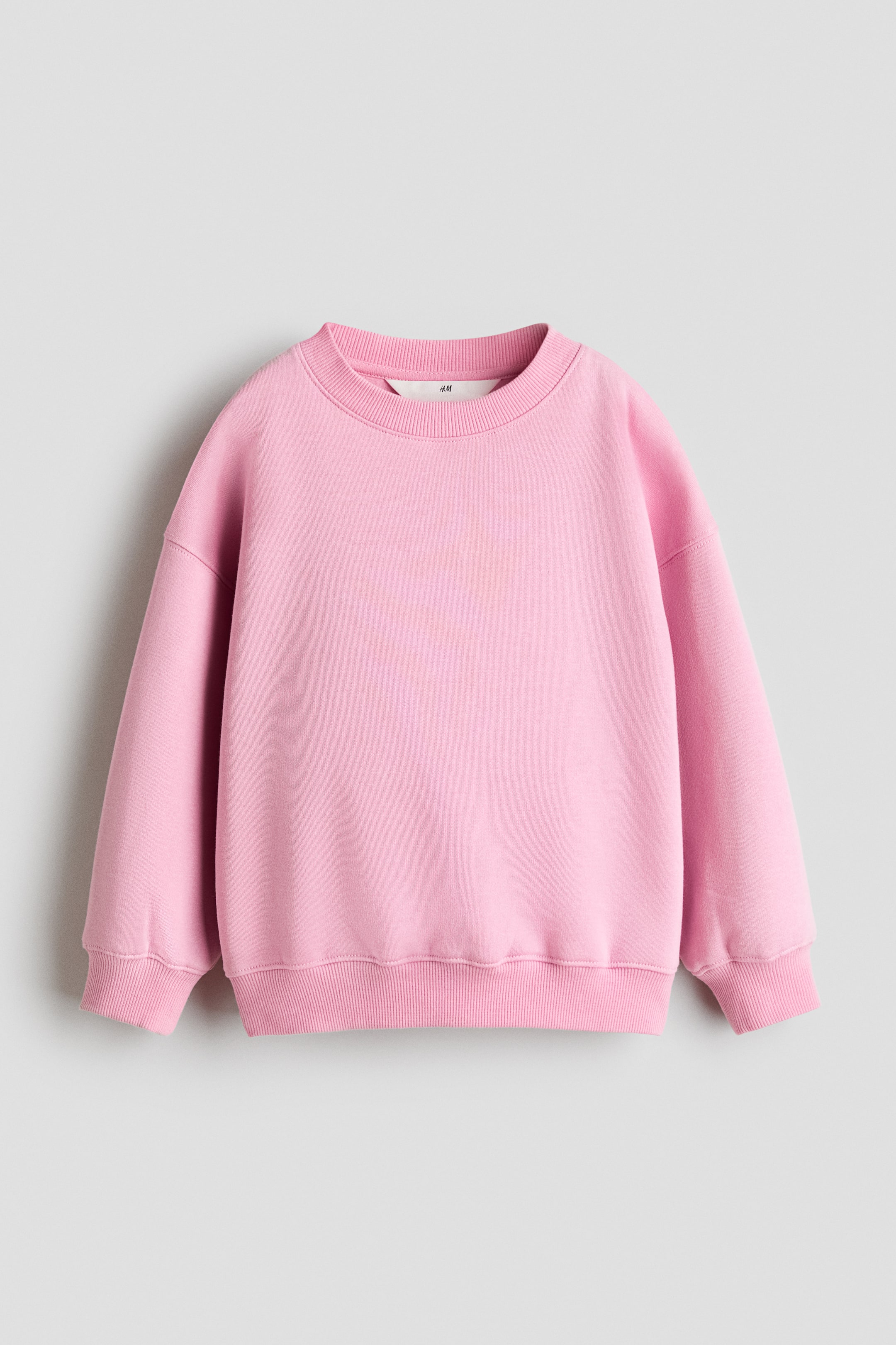 Größeres Bild anzeigen: Ein rosa Sweatshirt ist von vorne zu sehen und verfügt über einen runden, gerippt eingefassten Ausschnitt, überschnittene Schultern und lange Ärmel; es ist mit gerippten Bündchen und einem gerippten Saum versehen.