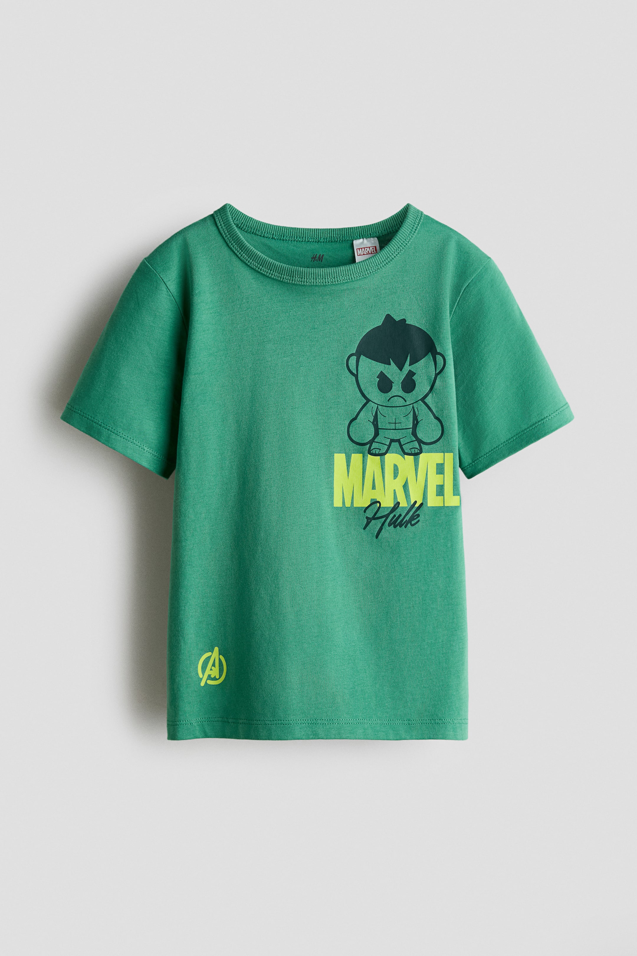 View larger image: A green short-sleeved t-shirt is presenting its FRONT, featuring a ribbed crew neck. On the front, a central graphic is appearing, which includes a black-outlined cartoon-style illustration of a Hulk character with dark green hair and eyebrows, "MARVEL" in bright yellow-green text, "Hulk" in dark green script, and a small bright yellow-green Avengers logo on the bottom left.