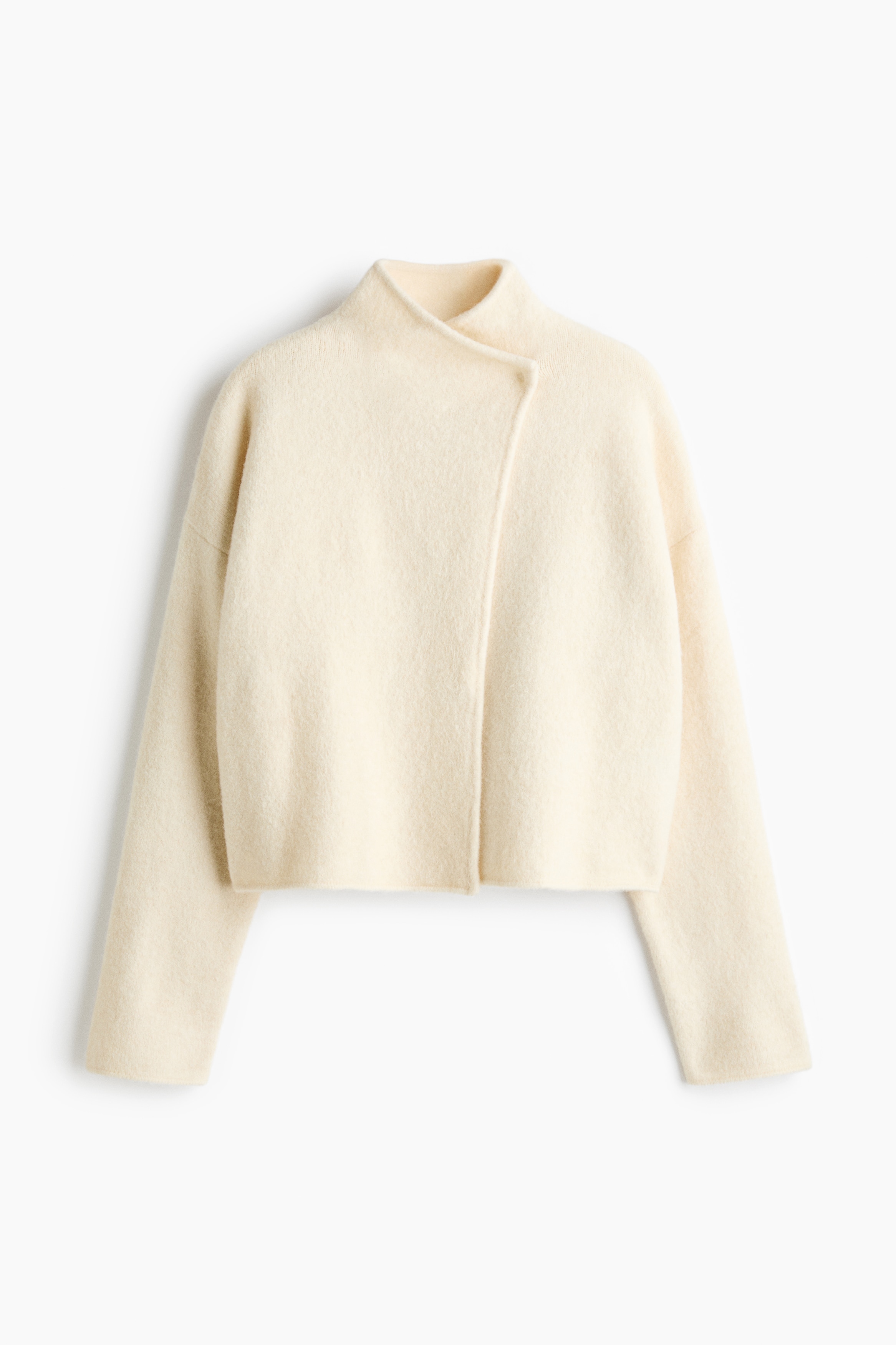 A short, cream-coloured cardigan in a soft, brushed knit is worn by the model, featuring a high stand collar, an asymmetrical wrapover front, and dropped shoulders. The loose-fit cardigan is layered over a black top and styled with leopard-print trousers.