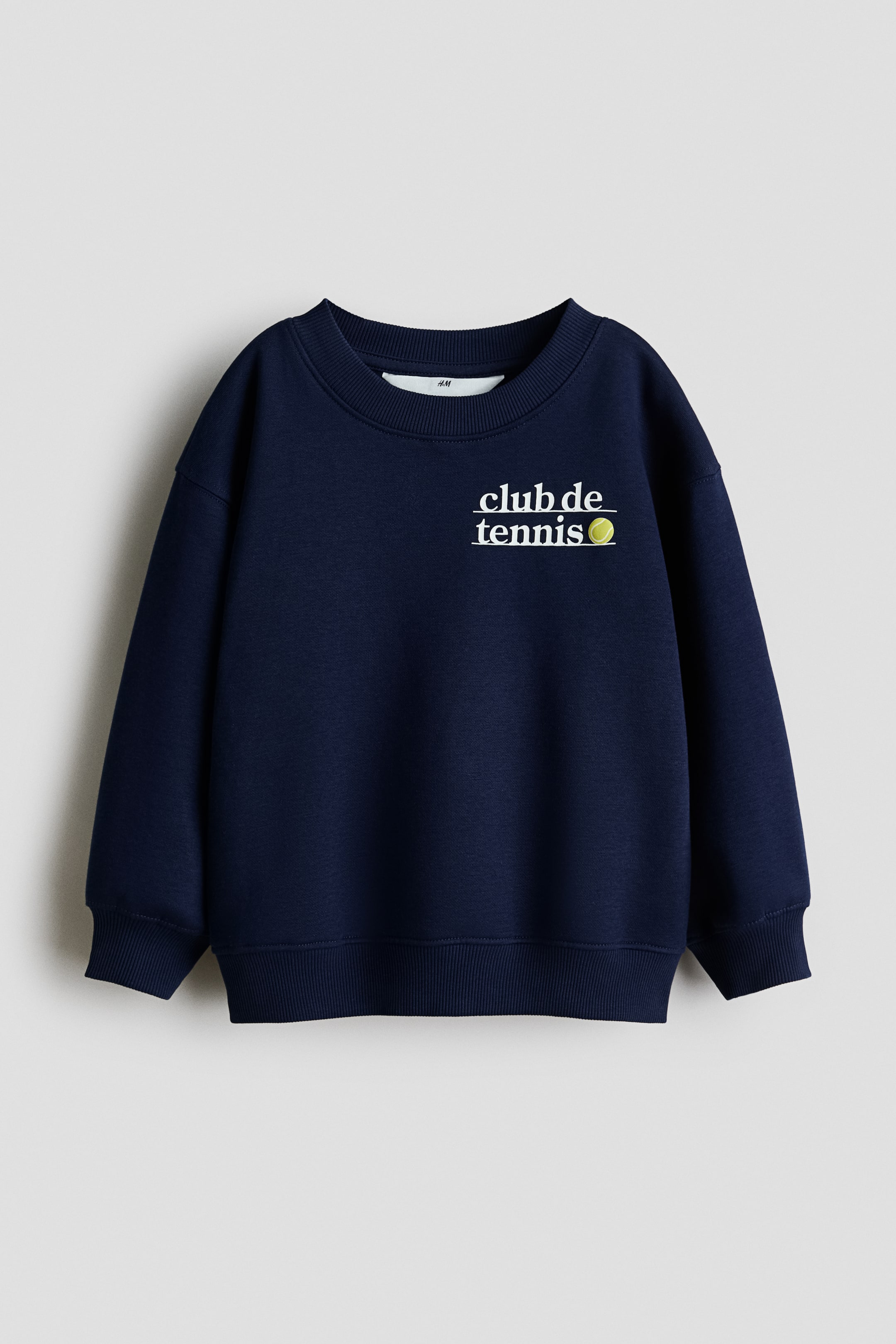 View larger image: A navy blue sweatshirt is displaying its front, featuring a white 'club de tennis' graphic with a yellow tennis ball on the chest, a round, rib-trimmed neckline, dropped shoulders, long sleeves, and ribbed cuffs and hem.