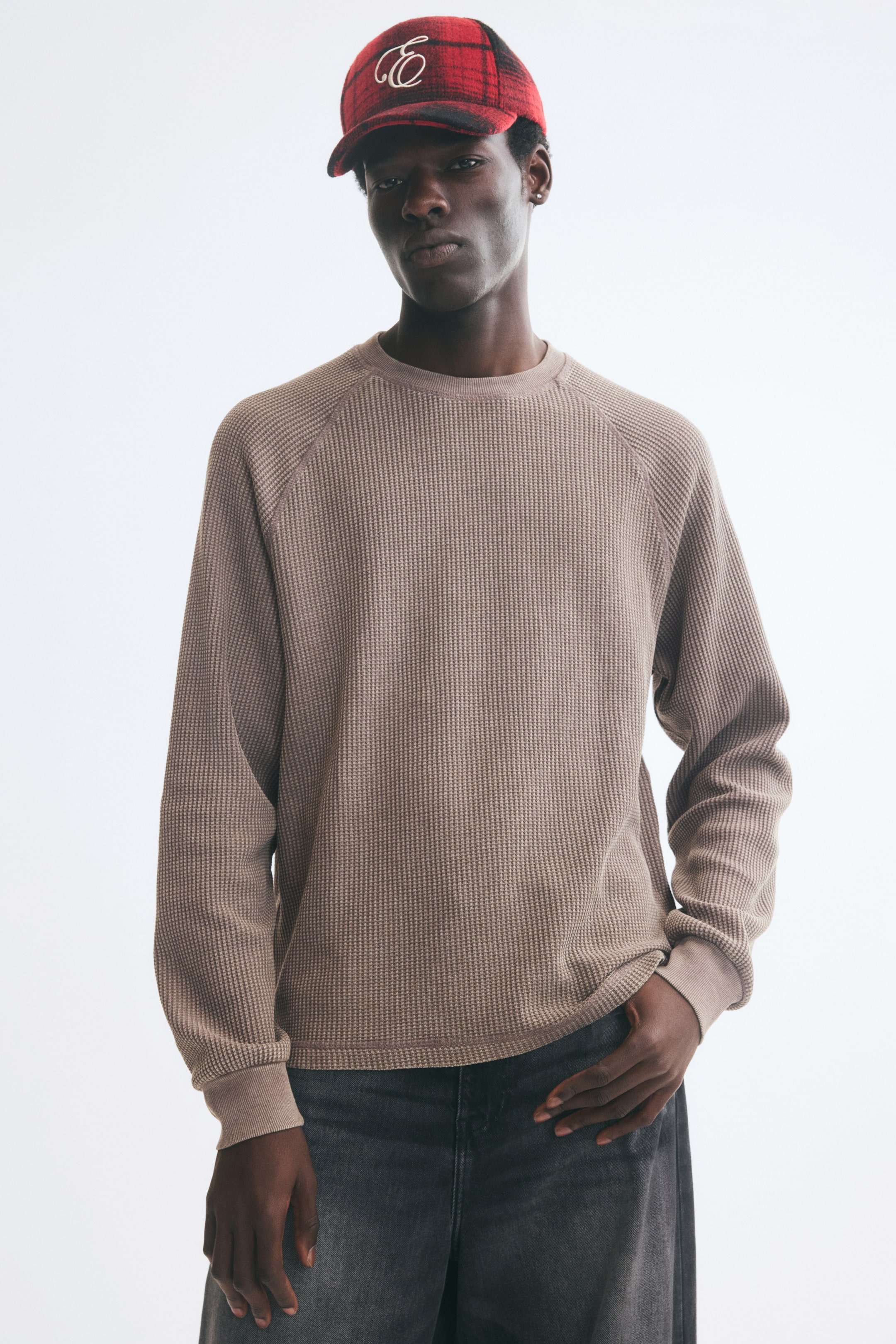 Grotere afbeelding bekijken: De model draagt een beige top met wafelstructuur en lange mouwen, met een ronde geribde halslijn, raglanmouwen met geribde boorden en een rechte zoom. Het model combineert de top met donkergrijze jeans en laat één hand rusten bij de voorzak.
