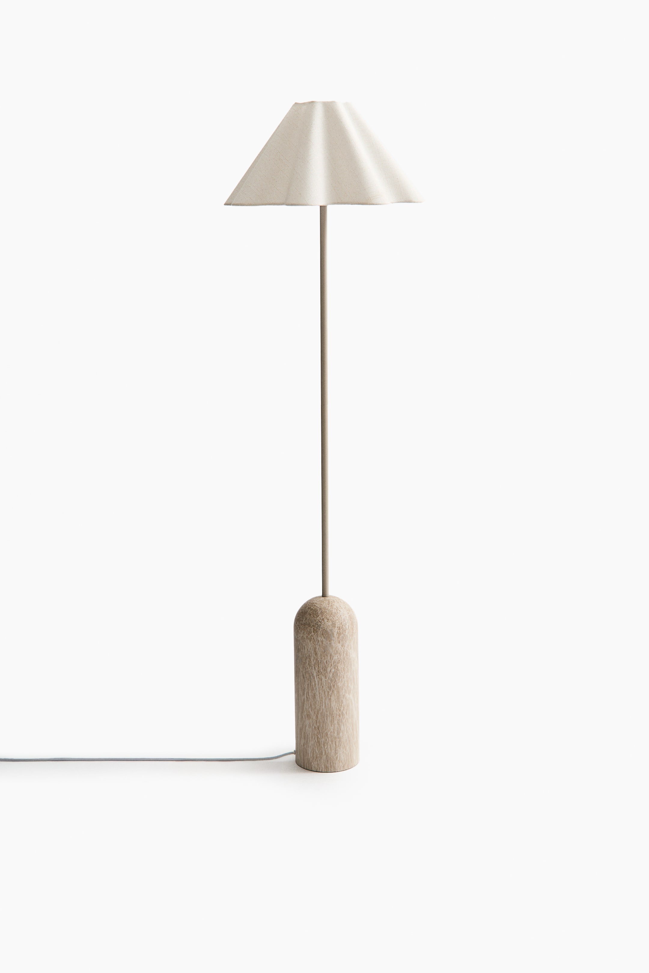 View larger image: This lamp features a light-coloured, fluted conical shade positioned at the top of a slender, neutral-toned stem. The stem rises from a textured, cylindrical base with a rounded top, and a power cord extends from the base.