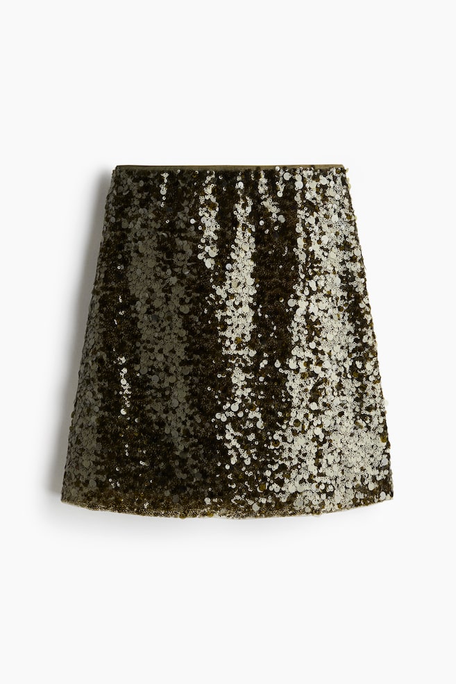 A mini skirt is lying flat, seen from the front. It is entirely covered in shimmering olive green and lighter gold sequins, creating a mottled effect across its slight A-line silhouette. - 1