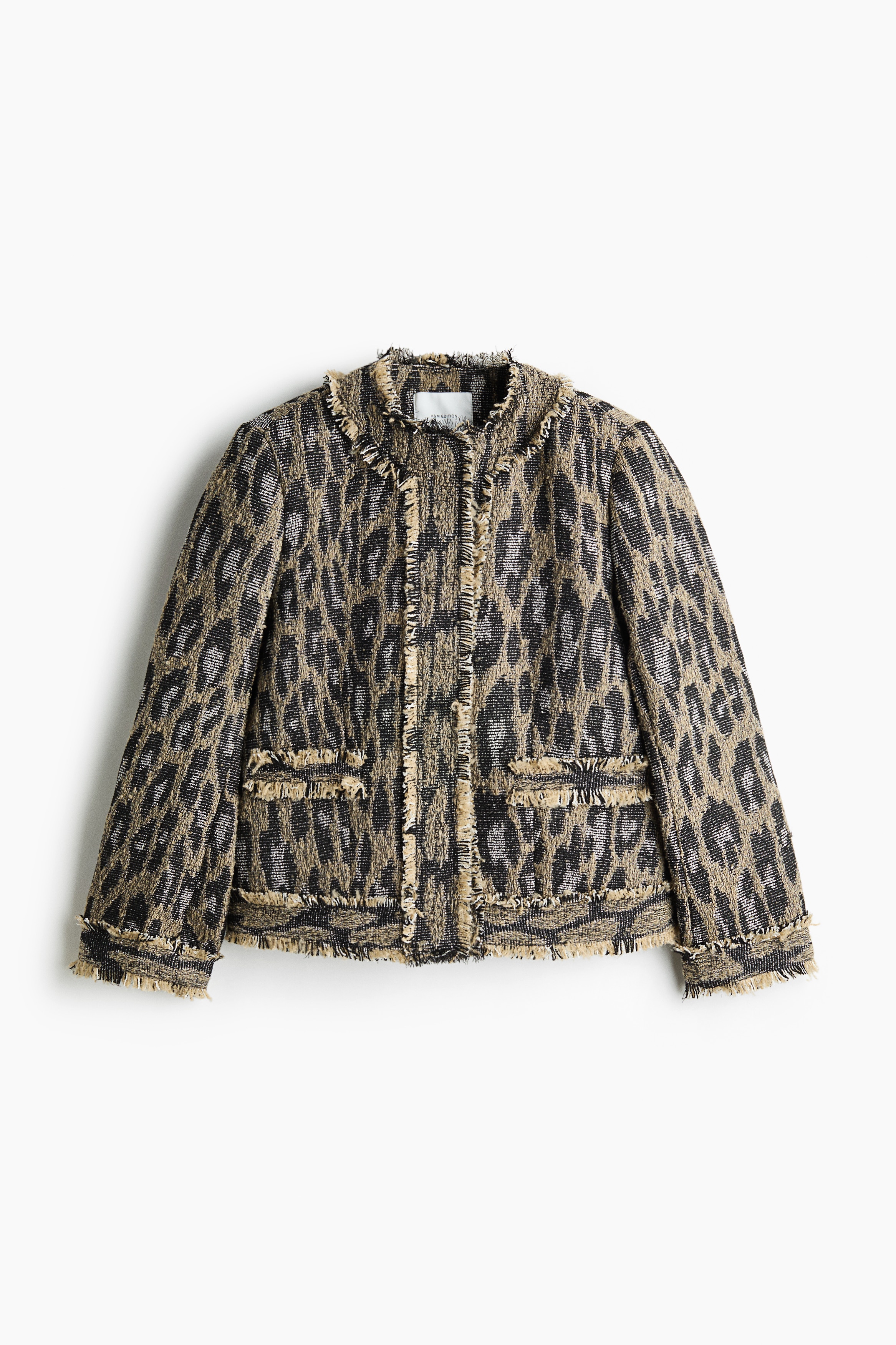 Eine Jacke in Jacquard-Webung mit schwarz-goldenem Mustermotiv und ausgefransten Saumdetails wird vom Model getragen. Das Model hÃ¤lt die vordere Ãffnung der Jacke und hebt so den strukturierten Stoff sowie die ausgefransten Kanten hervor.
