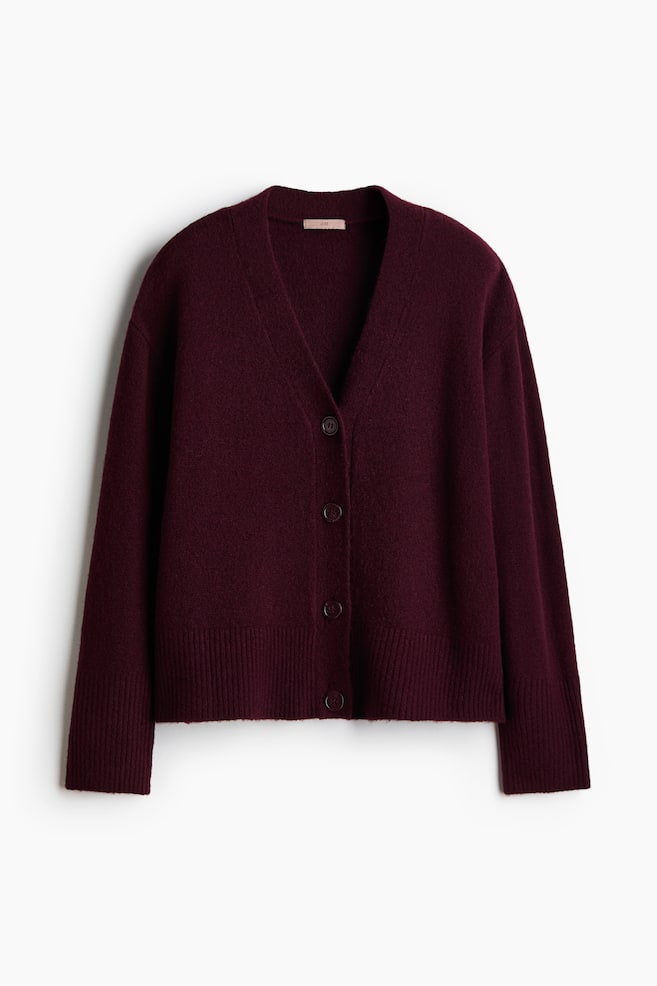 A dark burgundy knitted cardigan is shown from the front, featuring a deep V-neck, dropped shoulders, and long sleeves. It has a four-button front placket with ribbed detailing at the cuffs and hem. - 1