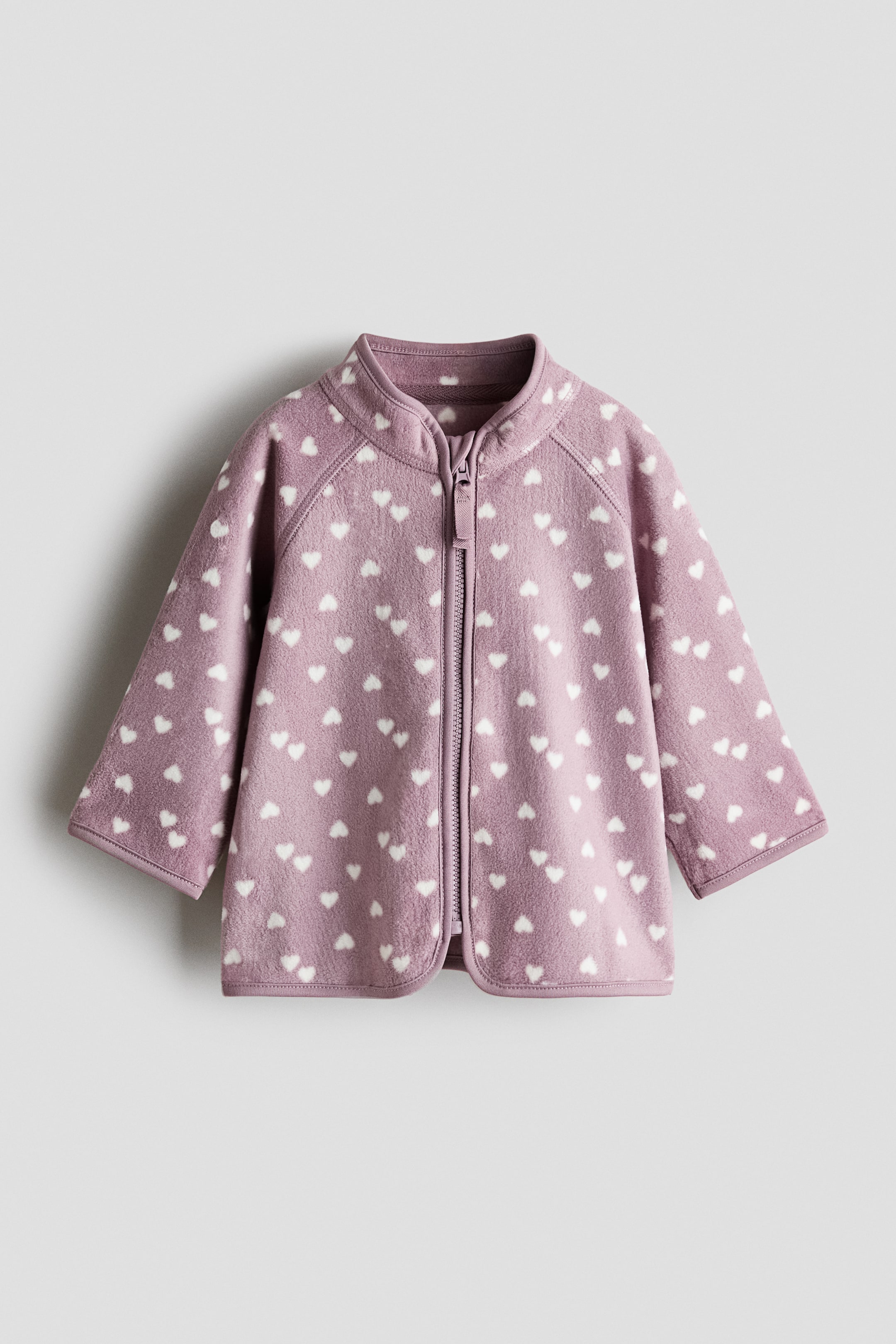 View larger image: A mauve fleece jacket showcases its front, adorned with white heart patterns. It features a stand-up collar, a zip down the front with a chin guard, raglan sleeves, and jersey trims at the collar, cuffs, and hem.