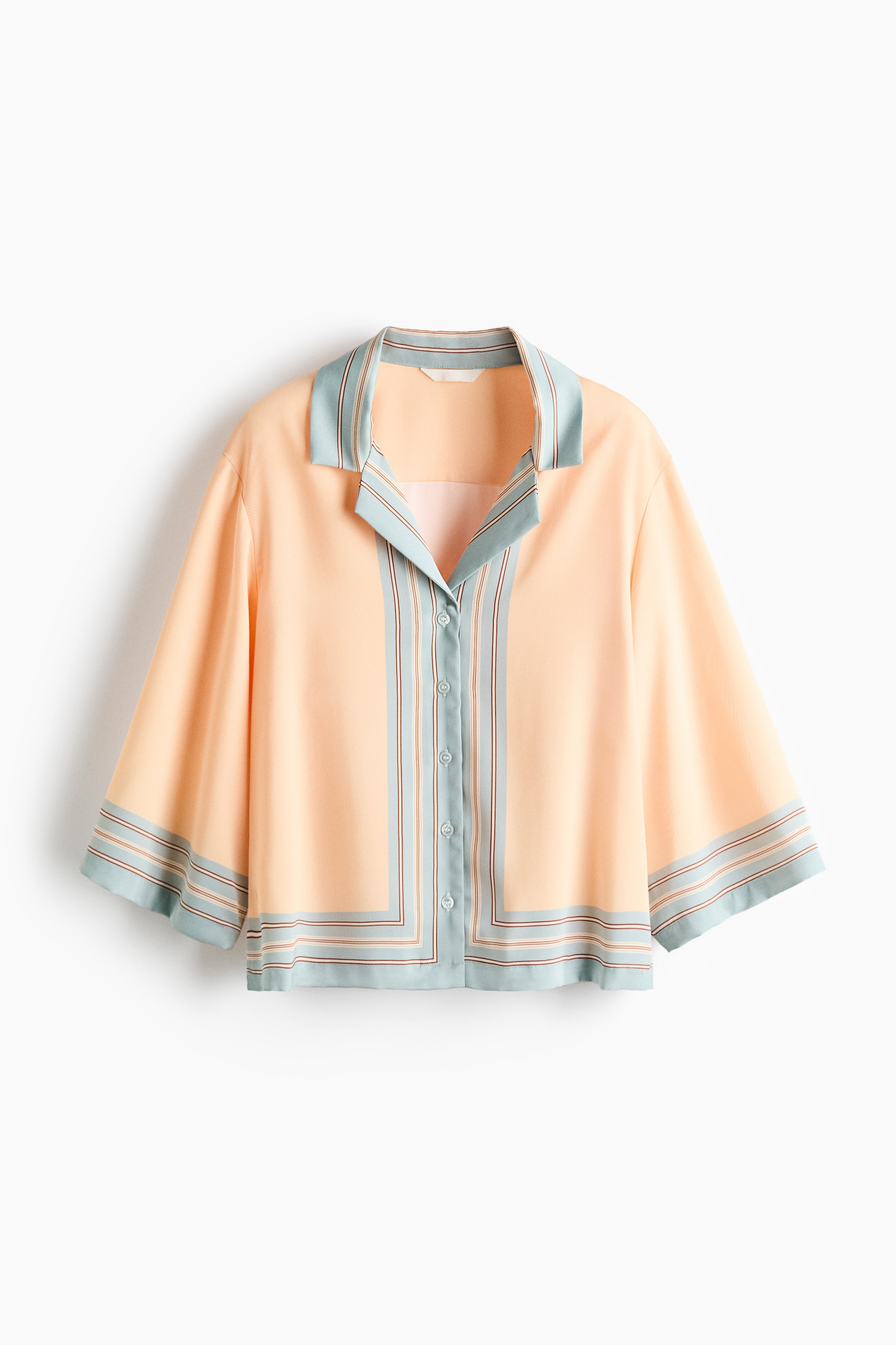 View larger image: A loose-fit peach twill shirt showcases its front, featuring a resort collar, a button-down front closure, elbow-length sleeves, and a straight-cut hem, all highlighted with light blue and striped borders.
