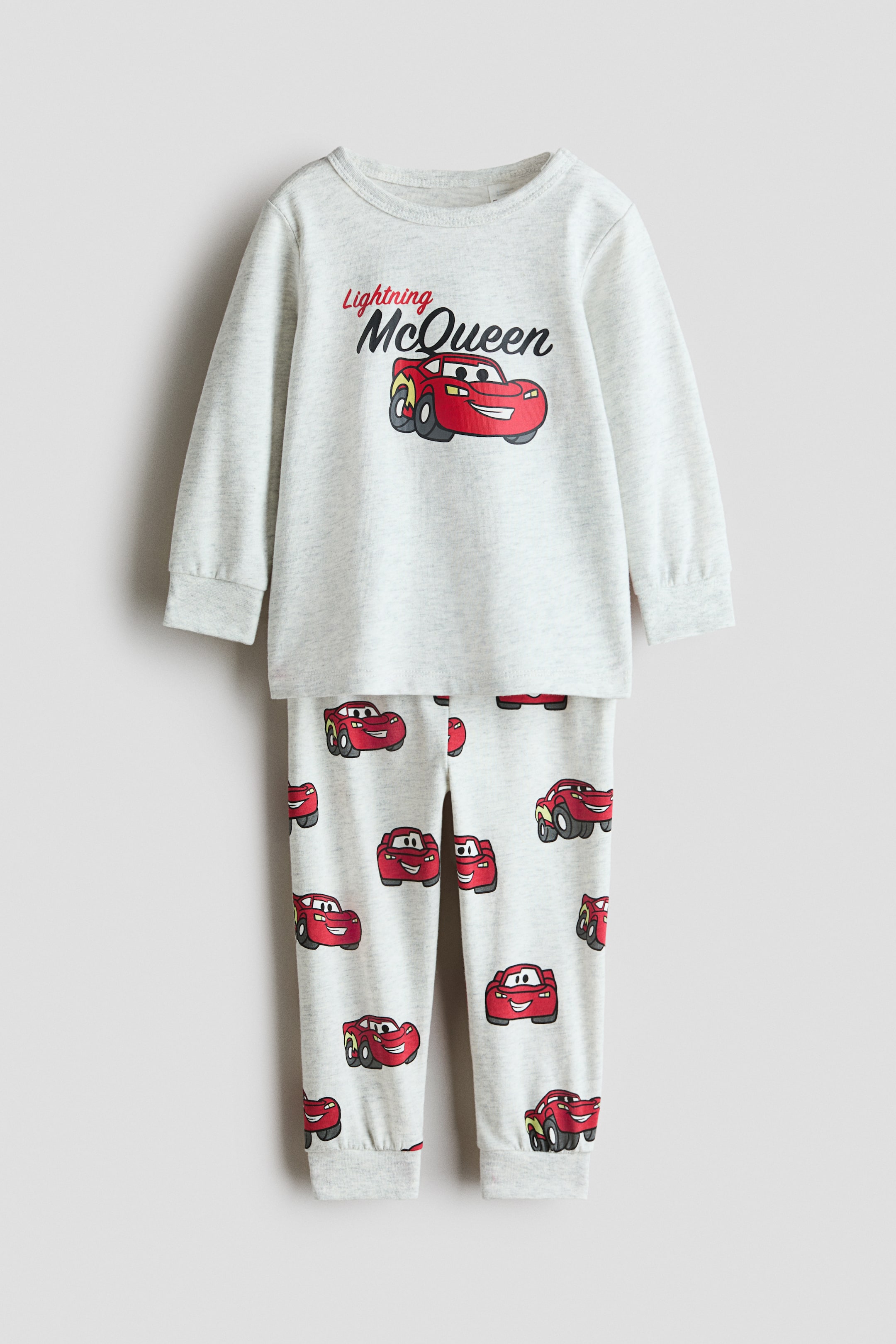 View larger image: Printed cotton pyjamas crafted from a light grey marl fabric, presented laid flat and facing forward. The long-sleeved top with a round neck showcases "Lightning McQueen" text and a large graphic of a red car, whilst the long bottoms feature a repeating pattern of smaller red cars and are finished with ribbed cuffs.