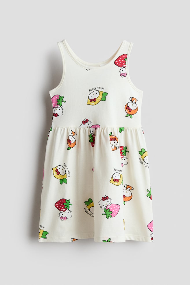 Das ärmellose Kleid wird von vorne gezeigt und präsentiert einen bunten Allover-Print mit fruchtigen Hello Kitty-Motiven auf einem cremeweißen Hintergrund. Es ist mit einem runden Halsausschnitt, schmalen Einfassungen an Hals- und Armausschnitten sowie einer gerafften Naht an der Taille gestaltet, die einen vollen Rock formt. - 1