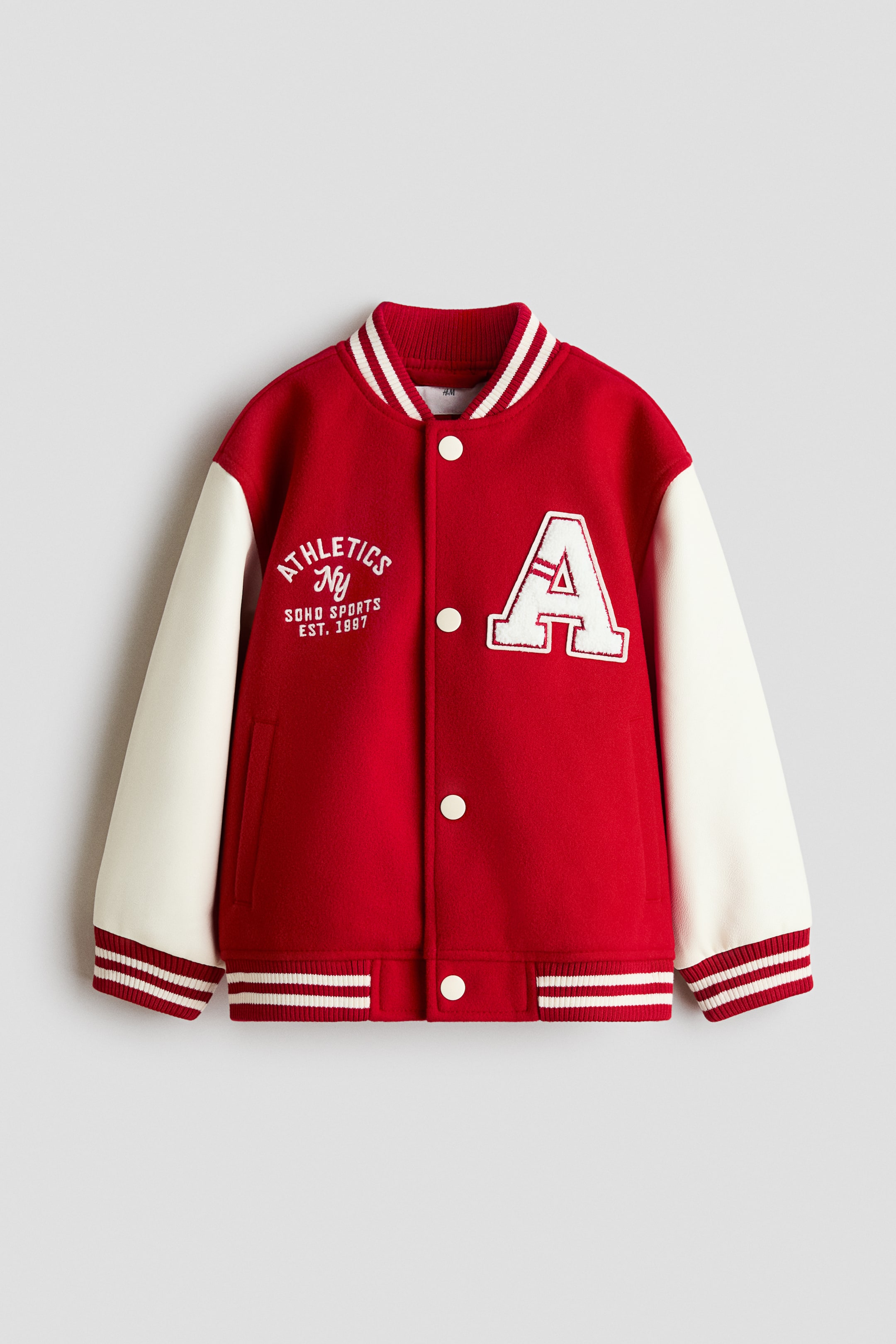 View larger image: The baseball jacket showcases a red felted fabric body complemented by contrasting cream-colored coated sleeves. It features a striped ribbed collar, cuffs, and hem, white press-studs along the front, and welt front pockets. Additionally, it displays the text 'ATHLETICS NY SOHO SPORTS EST. 1997' and a prominent 'A' motif on the chest.