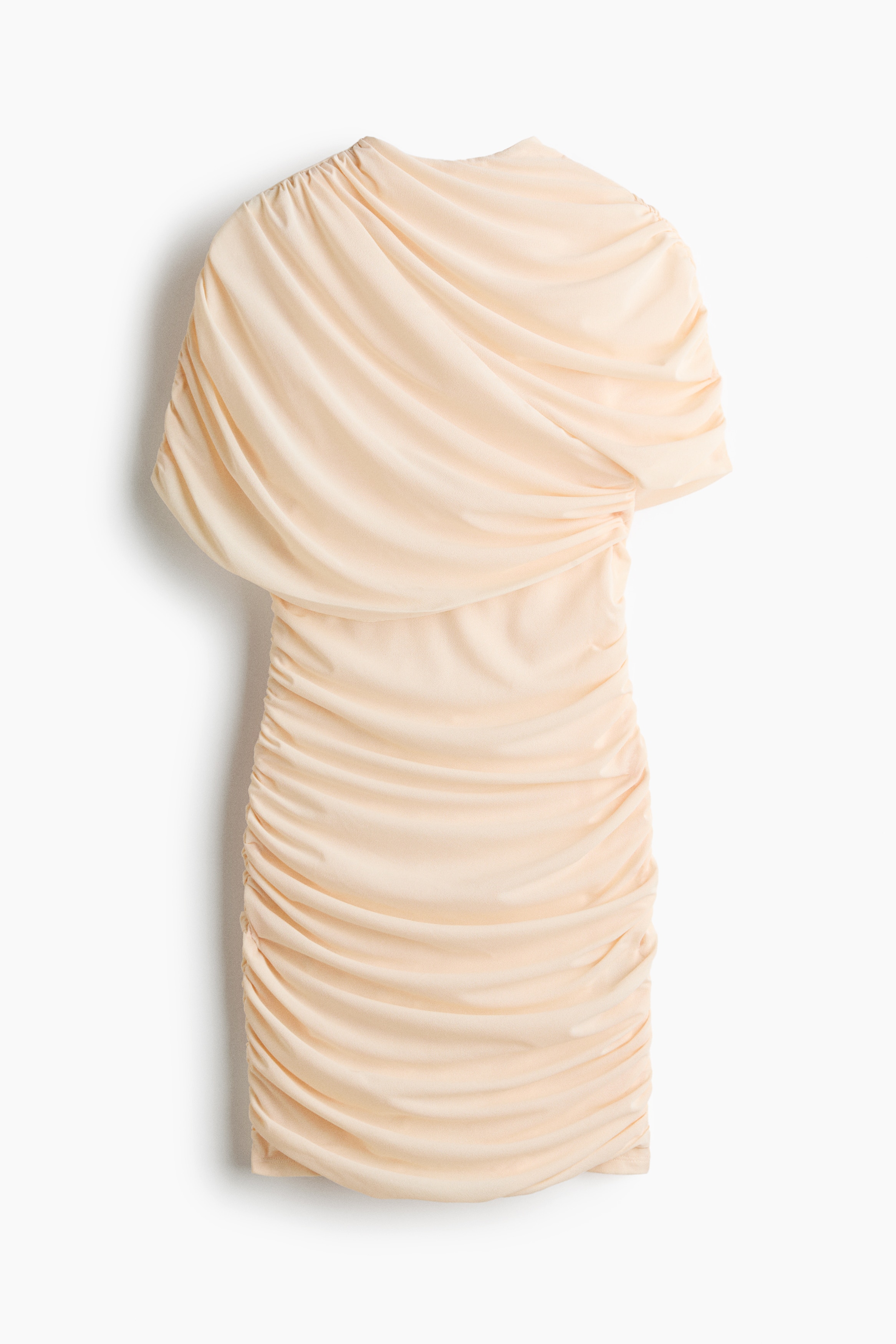 The model is wearing a cream-colored fitted mini dress in textured jersey, featuring extensive ruching and draped gathers. The dress has a high stand collar, an asymmetrical draped cape layer over the upper body, and a gathered short sleeve.
