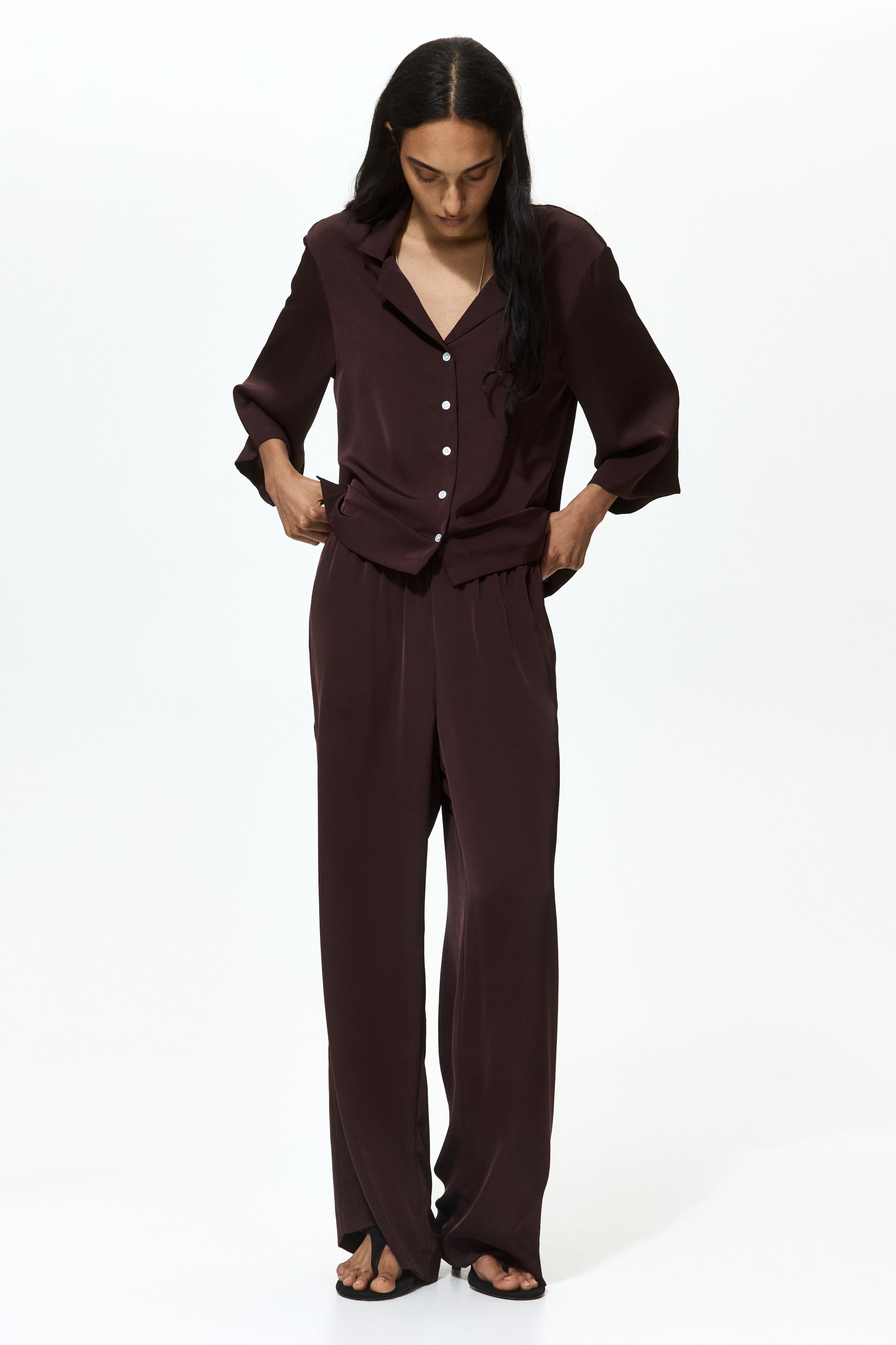 View larger image: Presenting a dark brown two-piece ensemble, consisting of a button-up shirt and wide-leg trousers. The shirt boasts a revere collar, three-quarter wide sleeves, white front buttons, and a left chest patch pocket. Meanwhile, the trousers feature an elasticated waist, side pockets, and a flowing full-length design.
