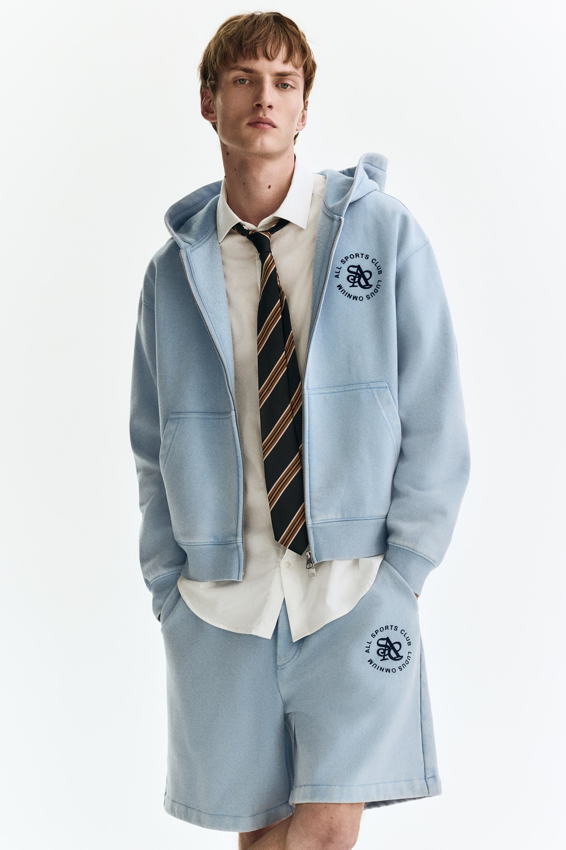 Zobrazit větší obrázek: Modelka má na sobě světle modré kraťasy z teplákoviny. Kraťasy mají šikmé boční kapsy, kruhové logo na levém stehně a pohodlný střih.