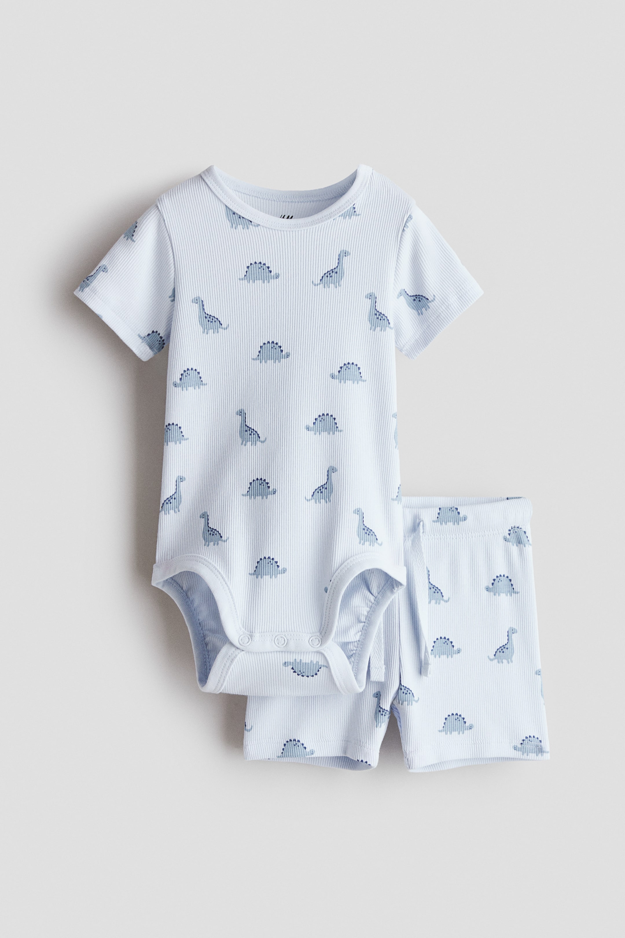 View larger image: A two-piece set featuring a short-sleeved bodysuit and a pair of shorts, both crafted from light blue ribbed cotton jersey with a dark blue dinosaur print. The front-facing bodysuit showcases a round neckline, a concealed snap on one shoulder, and snaps at the crotch, while the shorts feature covered elastic at the waist.