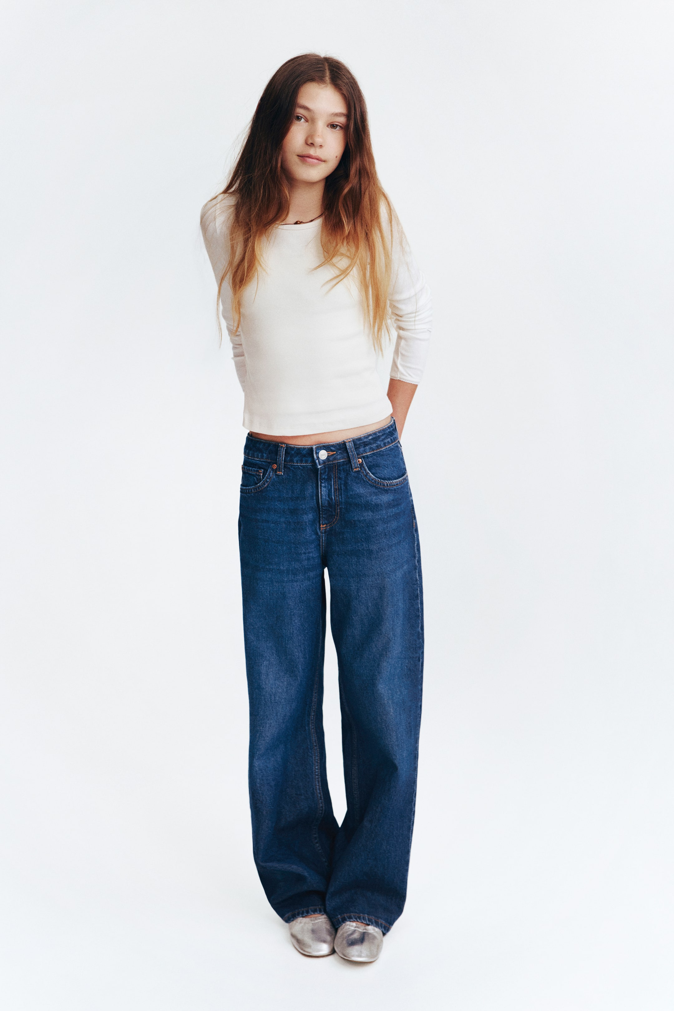 View larger image: This ensemble showcases a white ribbed long-sleeve top paired with blue high-waisted wide-leg denim jeans, viewed from a front-facing perspective. The top features a crew neck and a slightly cropped hem, while the jeans present a front button and zipper closure, complete with belt loops and visible pockets.