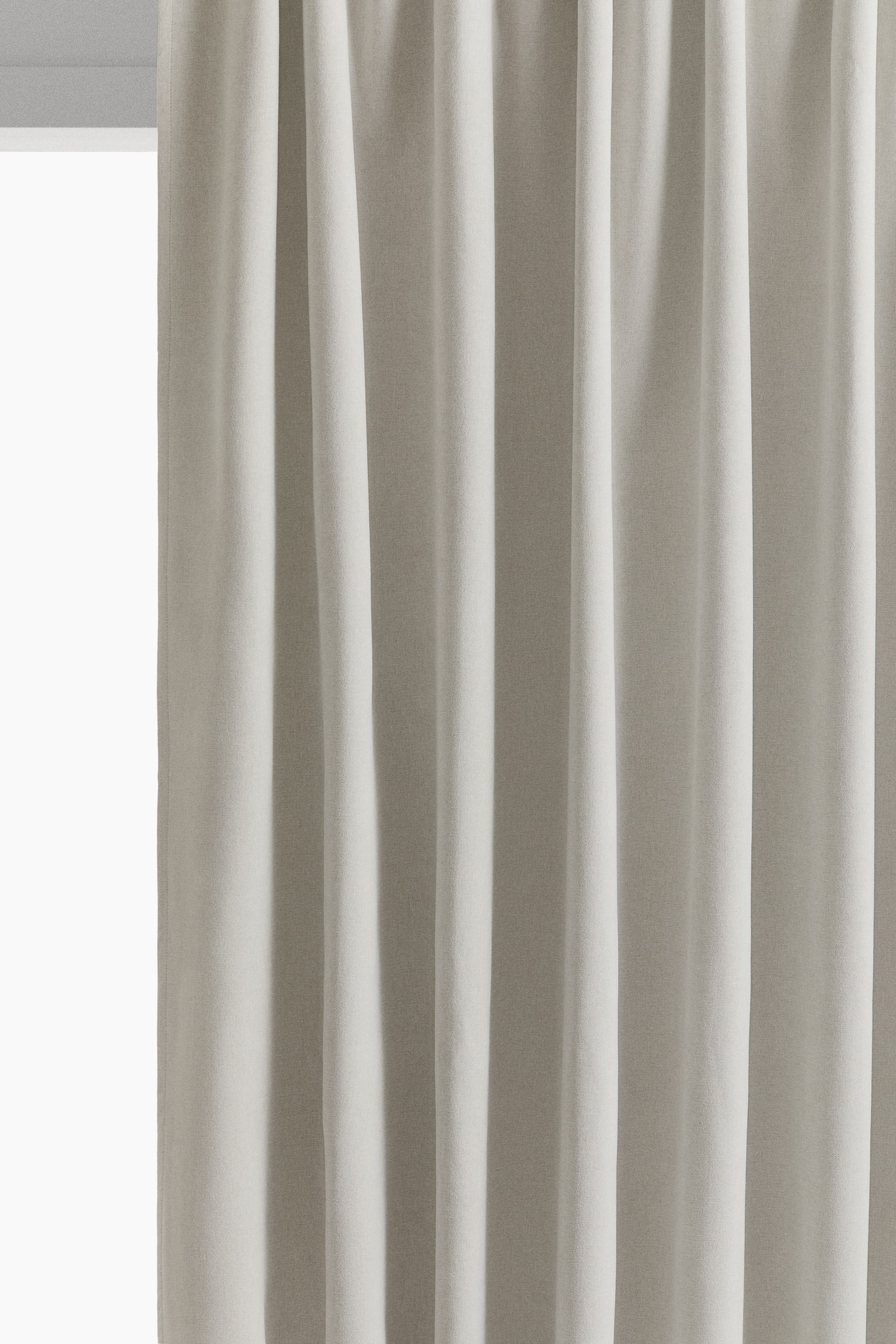 View larger image: A light beige chenille curtain hangs in dense, soft vertical folds in a front view, showcasing its thick, matte-textured fabric and uniform drape. The heavy fabric displays a soft, velvety surface that creates deep shadows within the folds.