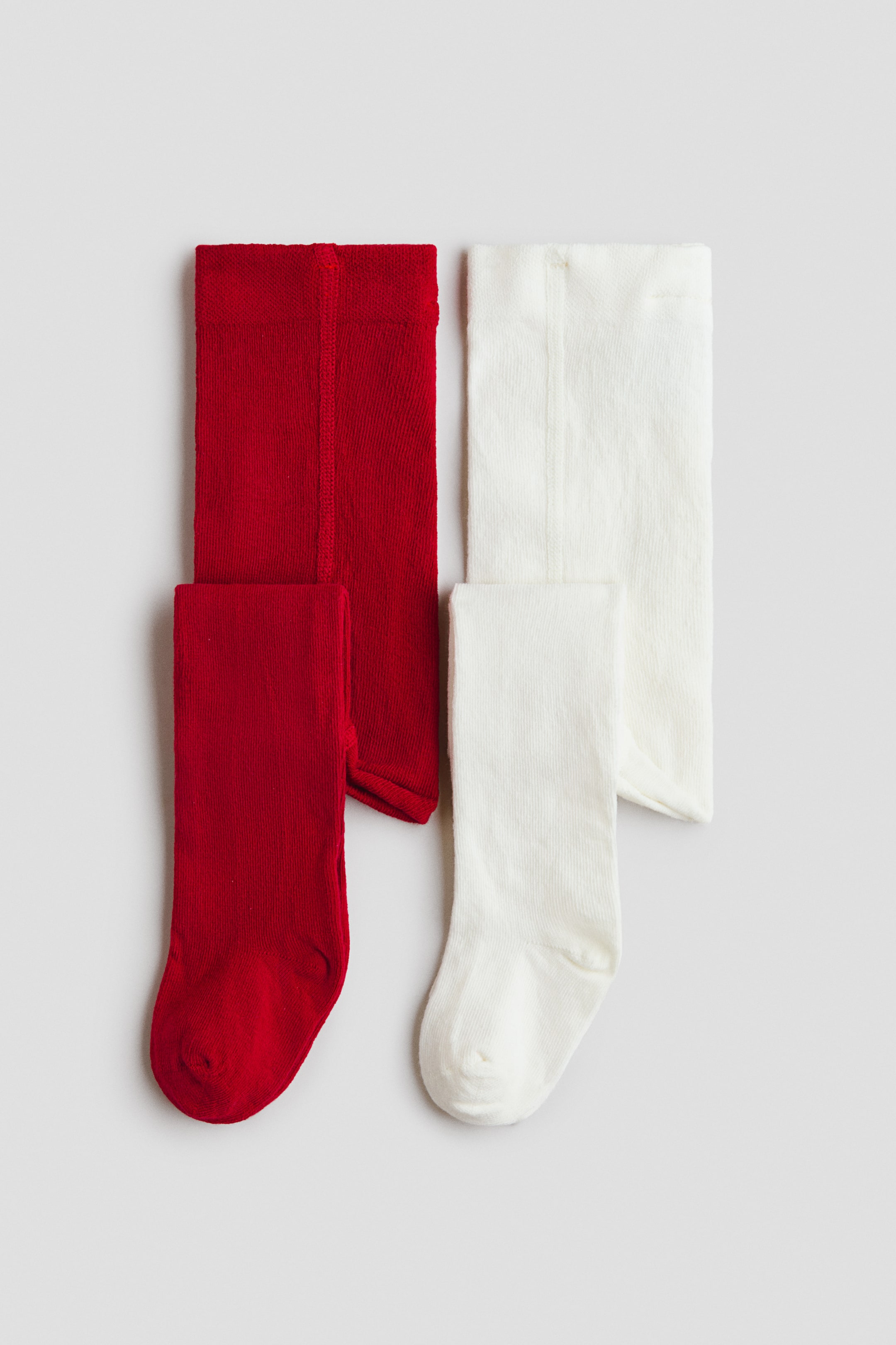 View larger image: Two pairs of tights are shown laid flat, one in red and one in off-white. Both pairs feature a soft, fine-knit cotton-blend texture and an elasticized waistband.
