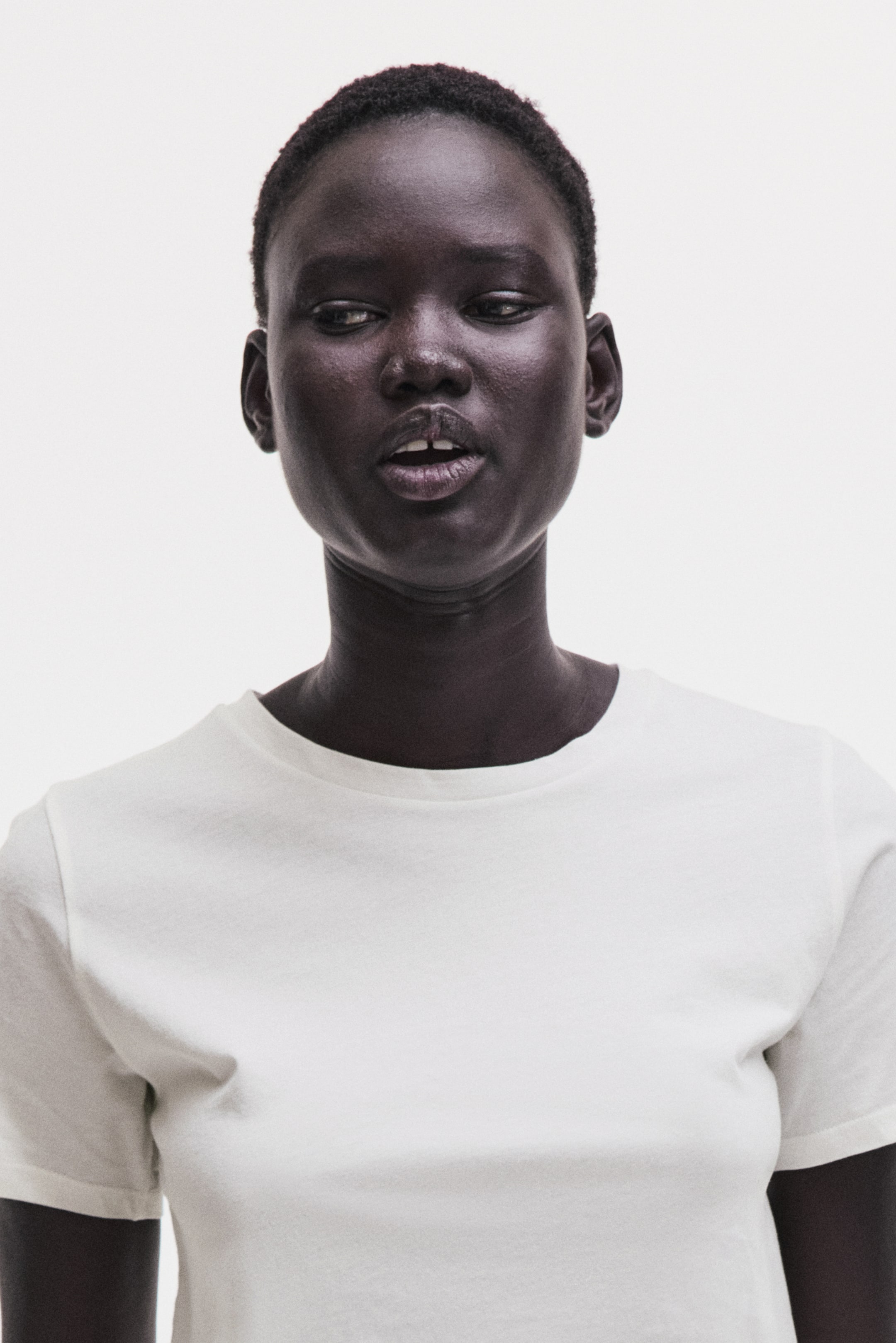 View larger image: A white T-shirt features a crew neck and short sleeves, with its plain fabric visible as it faces forward.