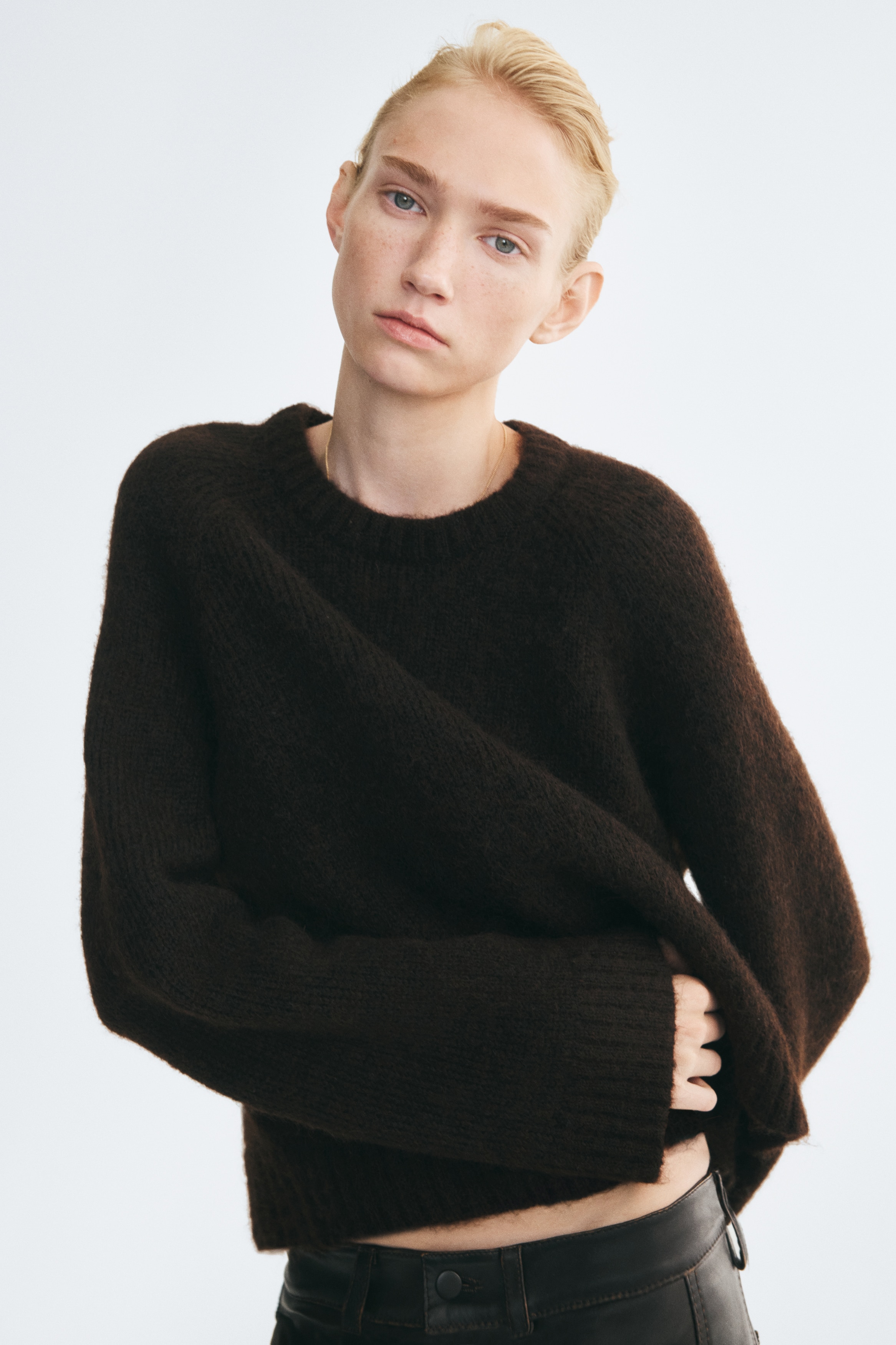Un maglione oversize marrone scuro in morbida maglia effetto peluche è mostrato frontalmente, con scollo rotondo rifinito a coste, maniche lunghe con polsini a coste e orlo a coste.