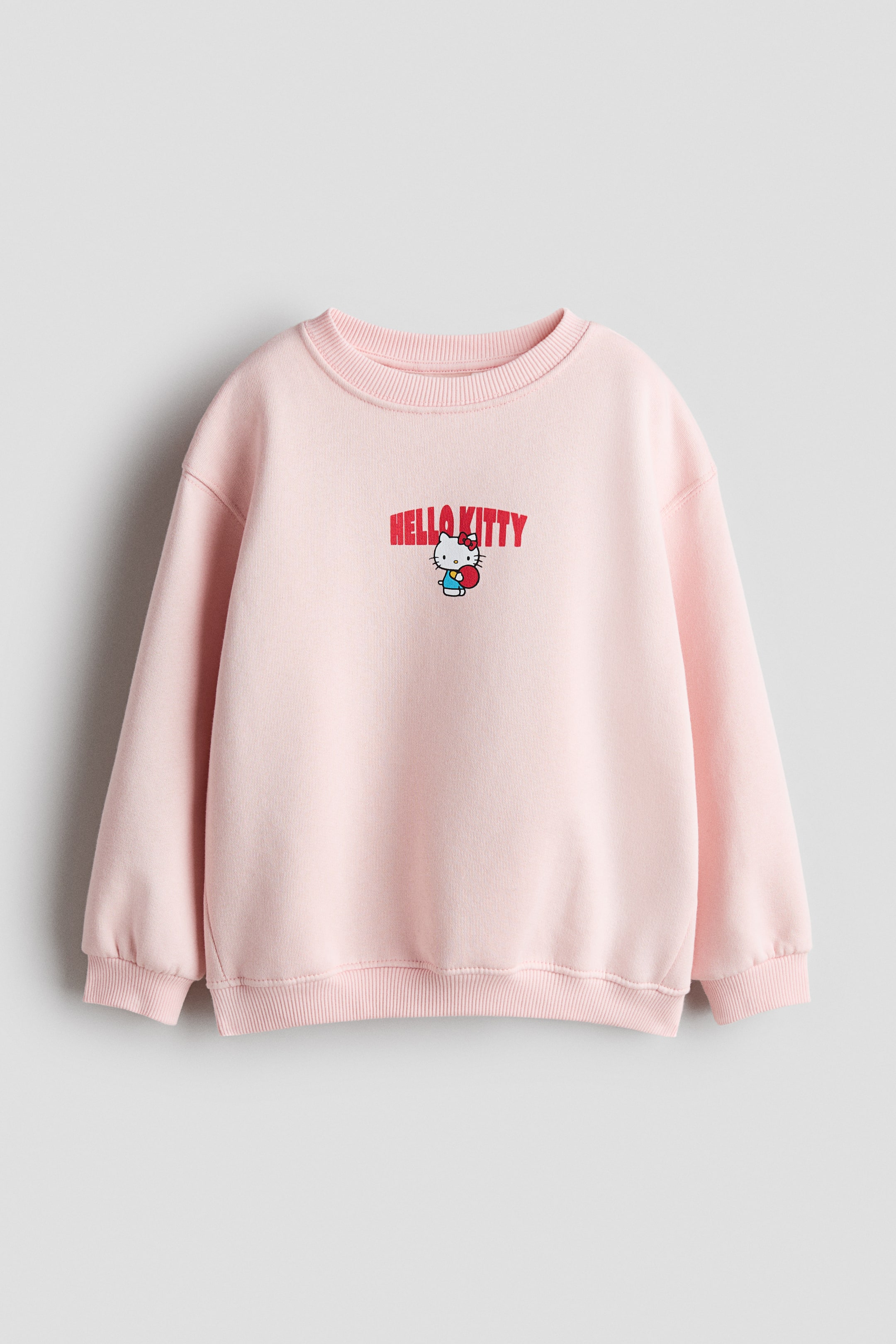 View larger image: A pink sweatshirt in sweatshirt fabric is showcasing its front view, featuring a 'Hello Kitty' print motif with red text and a character holding a red heart. It is crafted with a round, rib-trimmed neckline, dropped shoulders, long sleeves, and ribbing at the cuffs and hem.