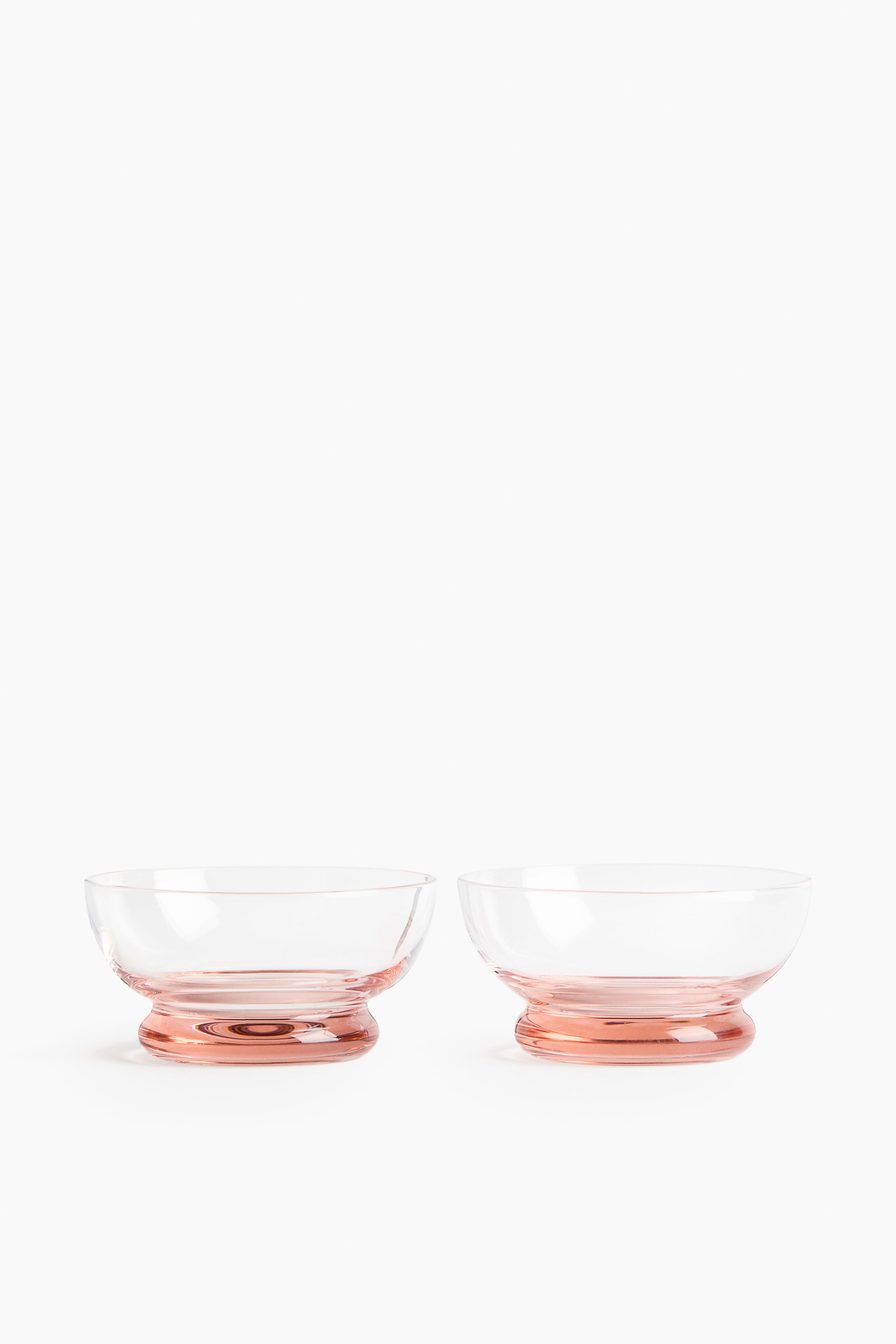 Visa större bild: Två handblåsta glasskålar med serveringsfunktion visar upp en mjukt rundad design. De har en djärv, tonad rosa bas och är vända FRAMÅT.
