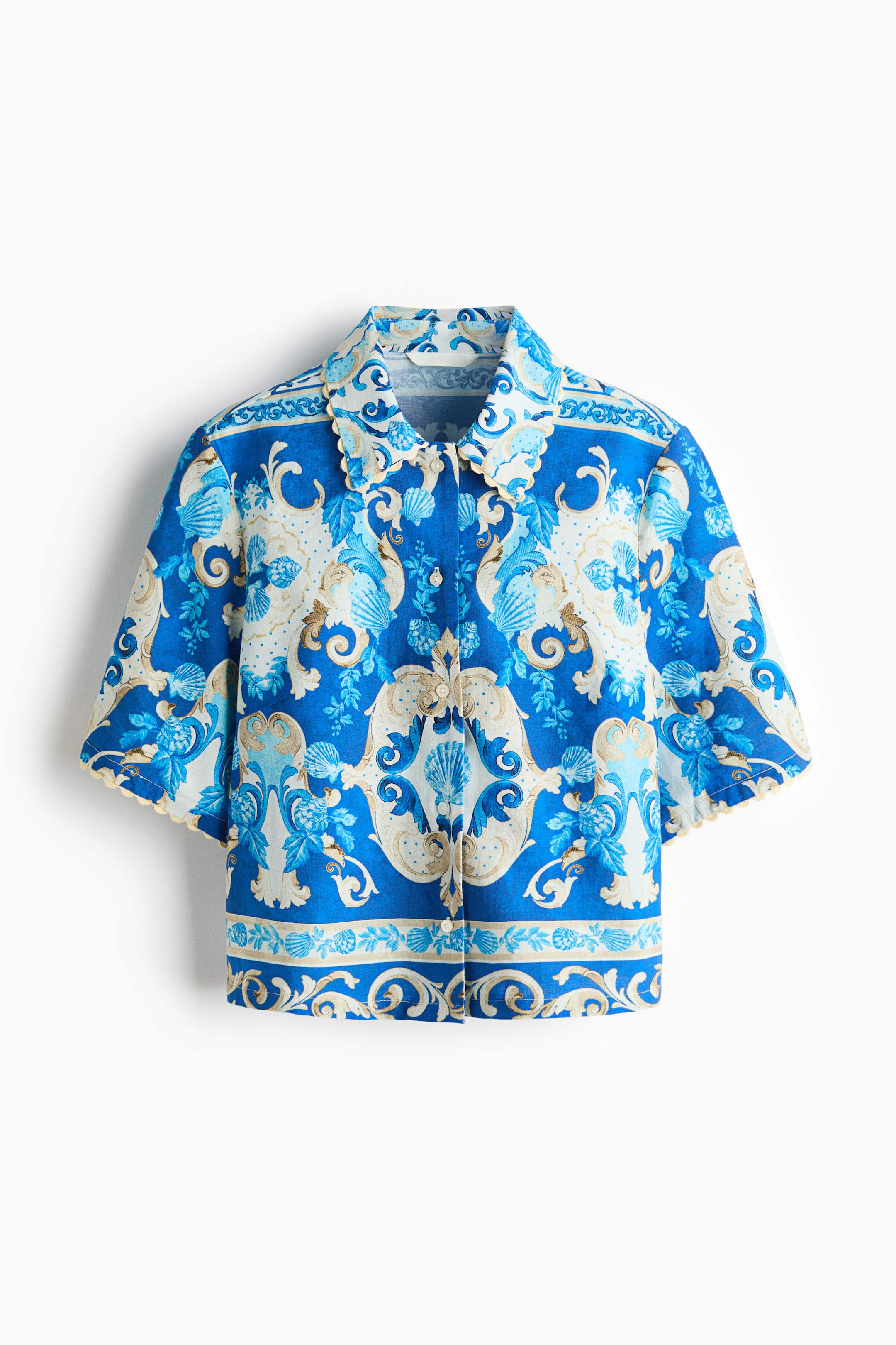 Ver imagem maior: Uma camisa de mangas curtas em azul e creme apresenta um padrão ornamentado em estilo barroco de conchas, volutas e folhagens, mostrado de frente. Possui uma gola com bordas onduladas, punhos de mangas curtas ondulados e um fecho frontal com botões brancos.